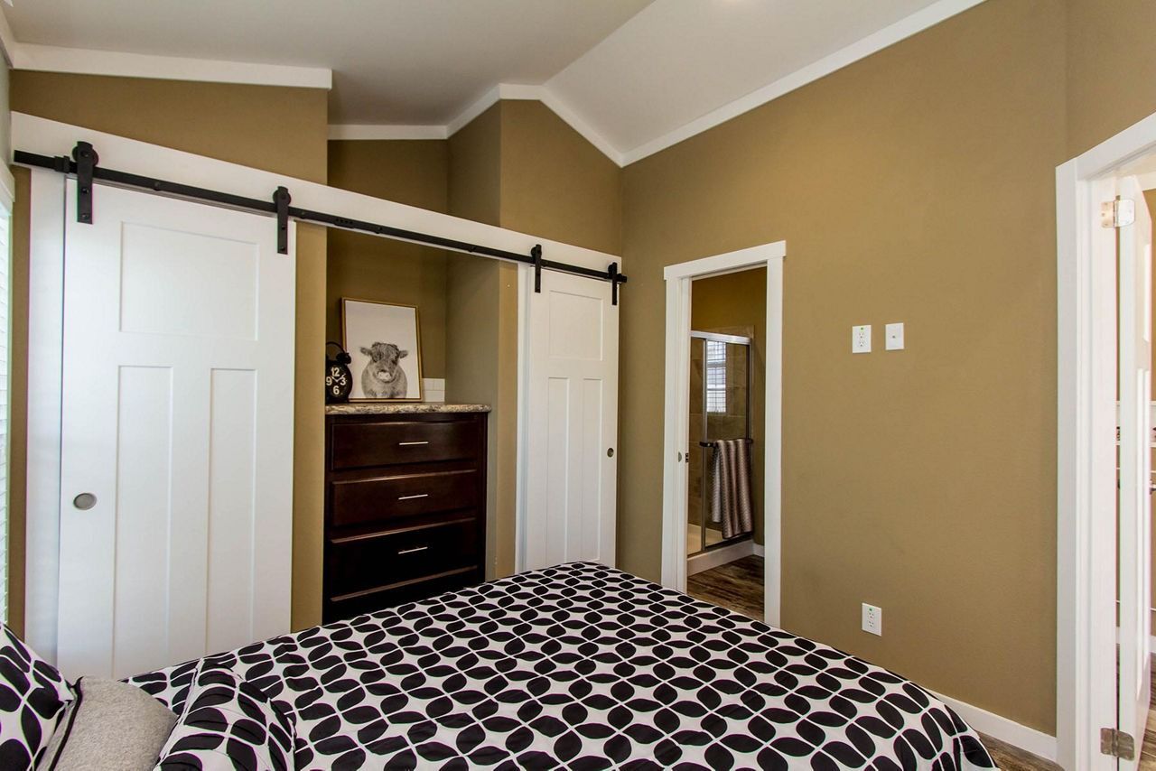 Bedroom with black-and-white patterned bedspread, sliding barn door, dresser, and tan walls