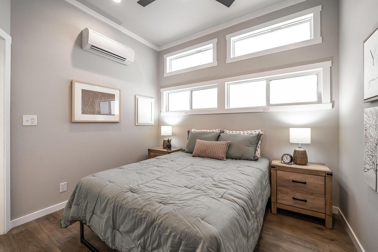 Bright bedroom with gray walls, a made bed, wood nightstands, and high windows above the bed