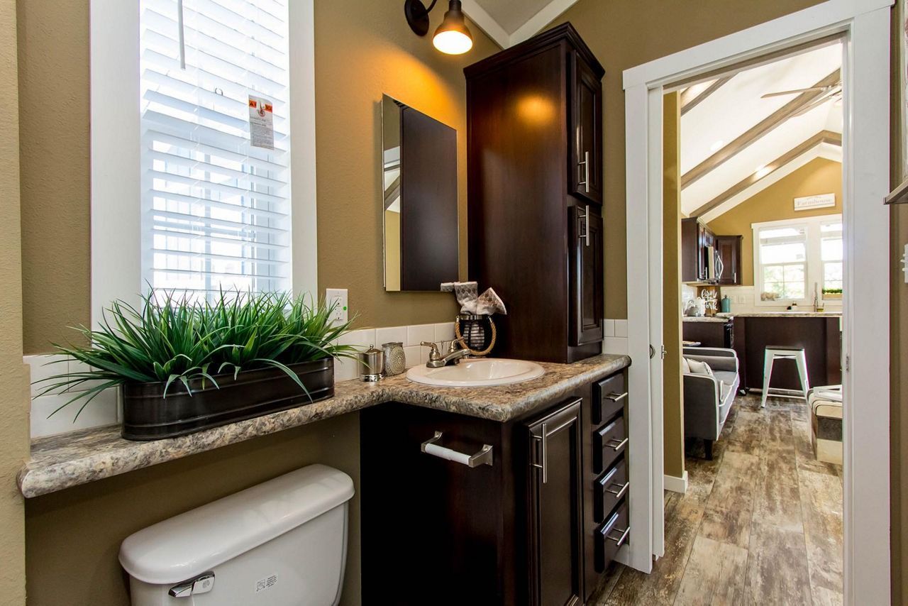 Small bathroom vanity with granite counter, black cabinets, and open doorway to a bright adjoining room.