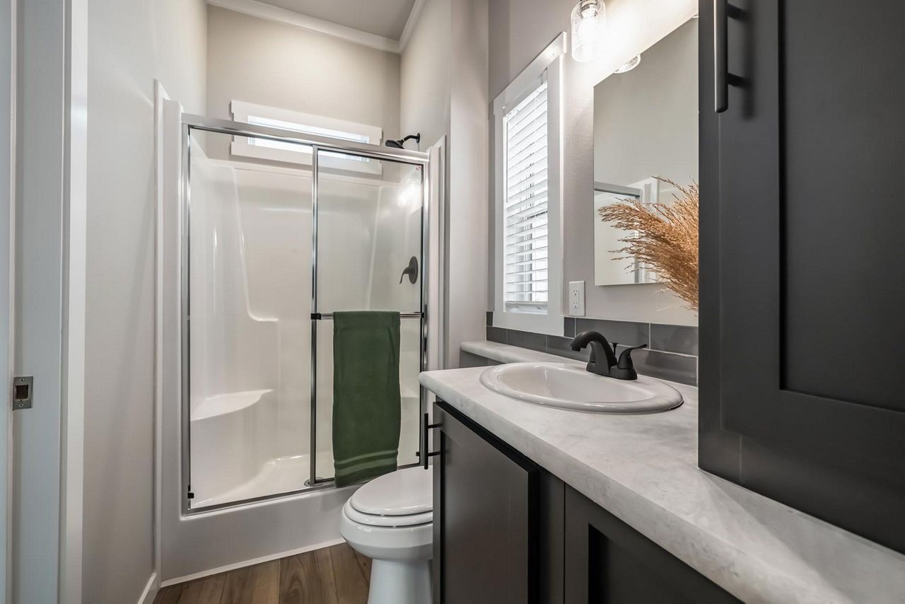 Compact bathroom with glass shower, toilet, and vanity sink in a narrow, light-gray space