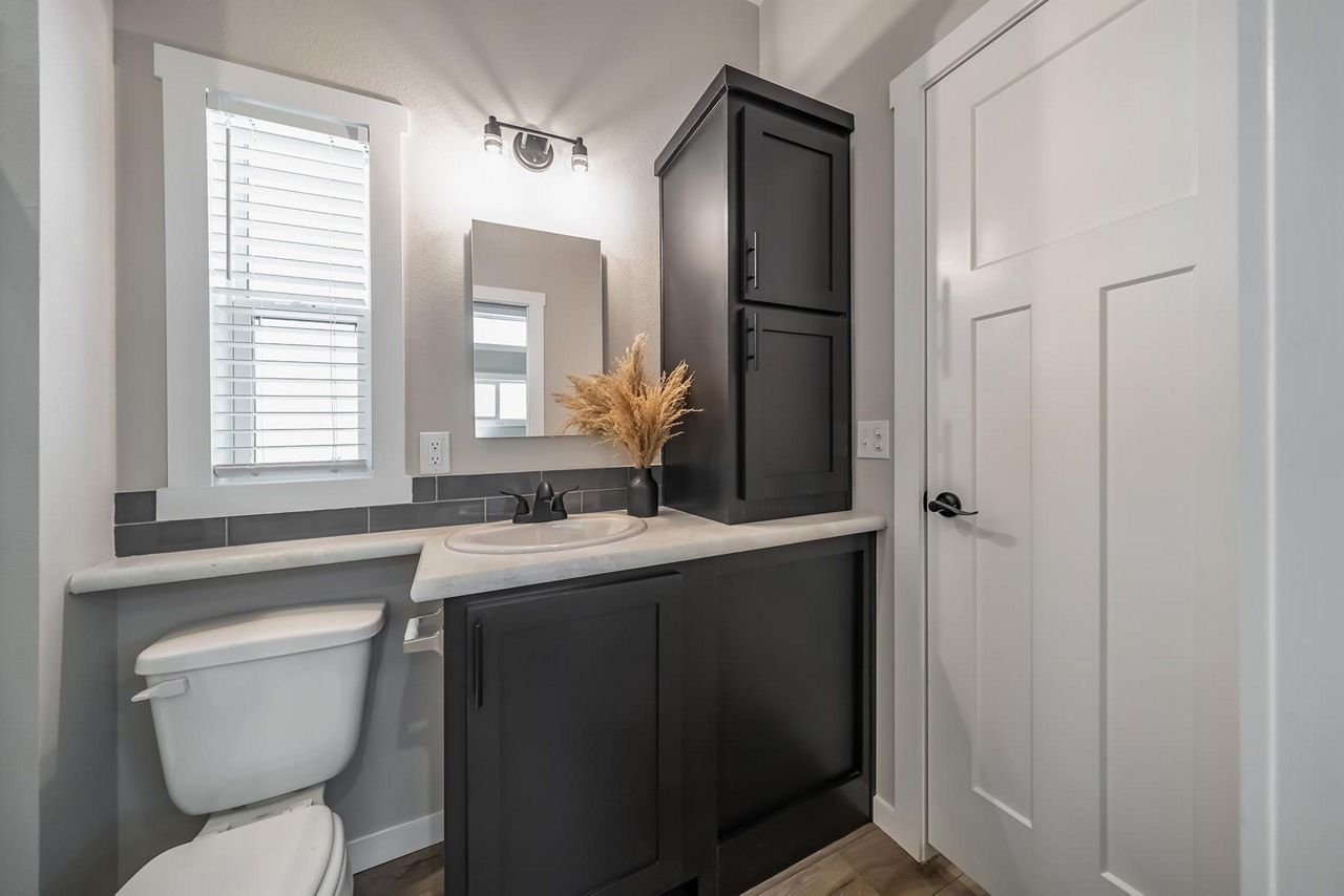 Modern bathroom vanity with dark cabinets, white countertop, mirror, window, and wall cabinet.