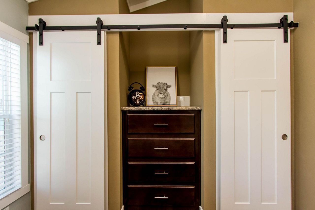 Open closet with sliding white doors framing a dark wood dresser in a beige room