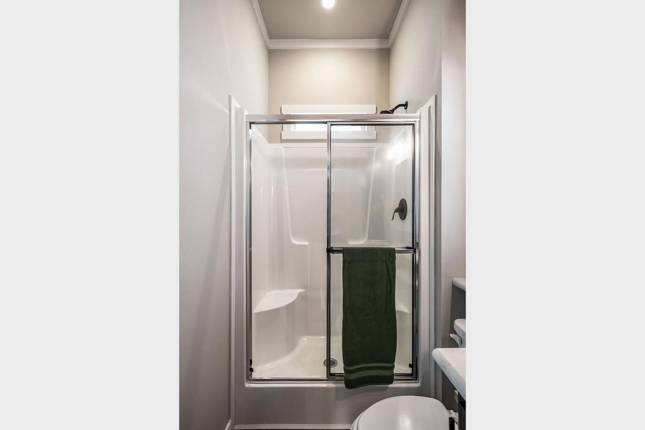 Small bathroom with a glass shower, white walls, and a green towel hanging on the door.