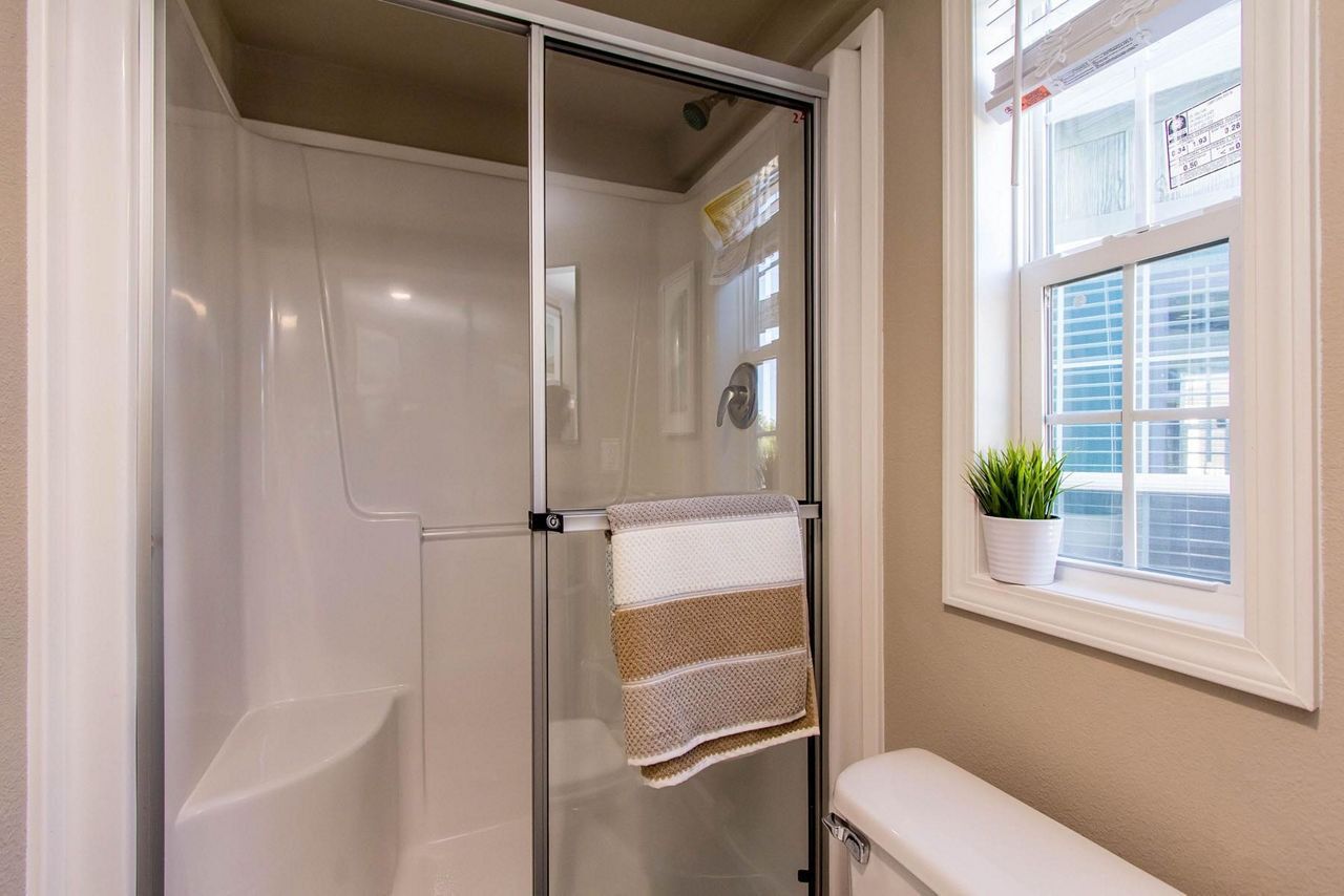 Small bathroom with a glass shower, beige walls, and a window beside a towel rack.
