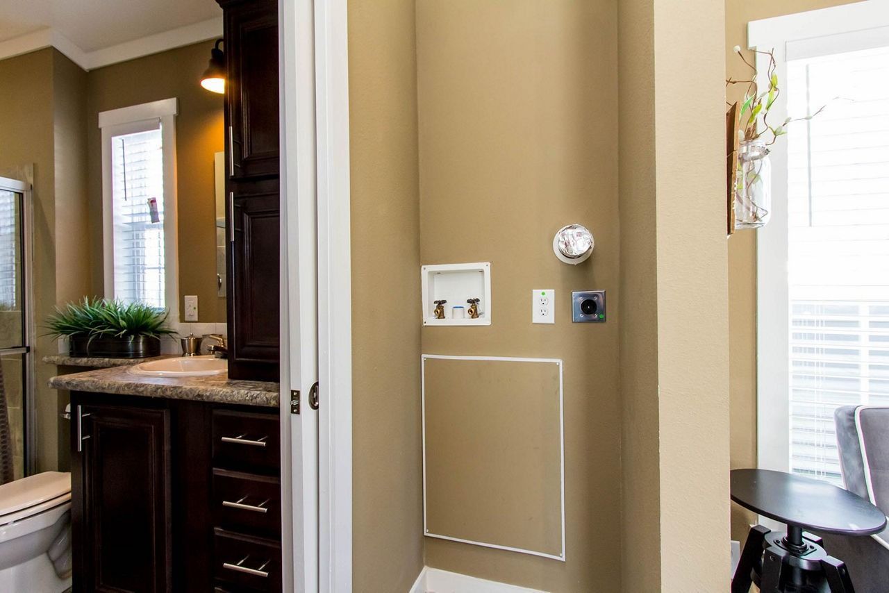 Hallway wall with thermostat, switches, and utility panel beside a bathroom vanity and window blinds
