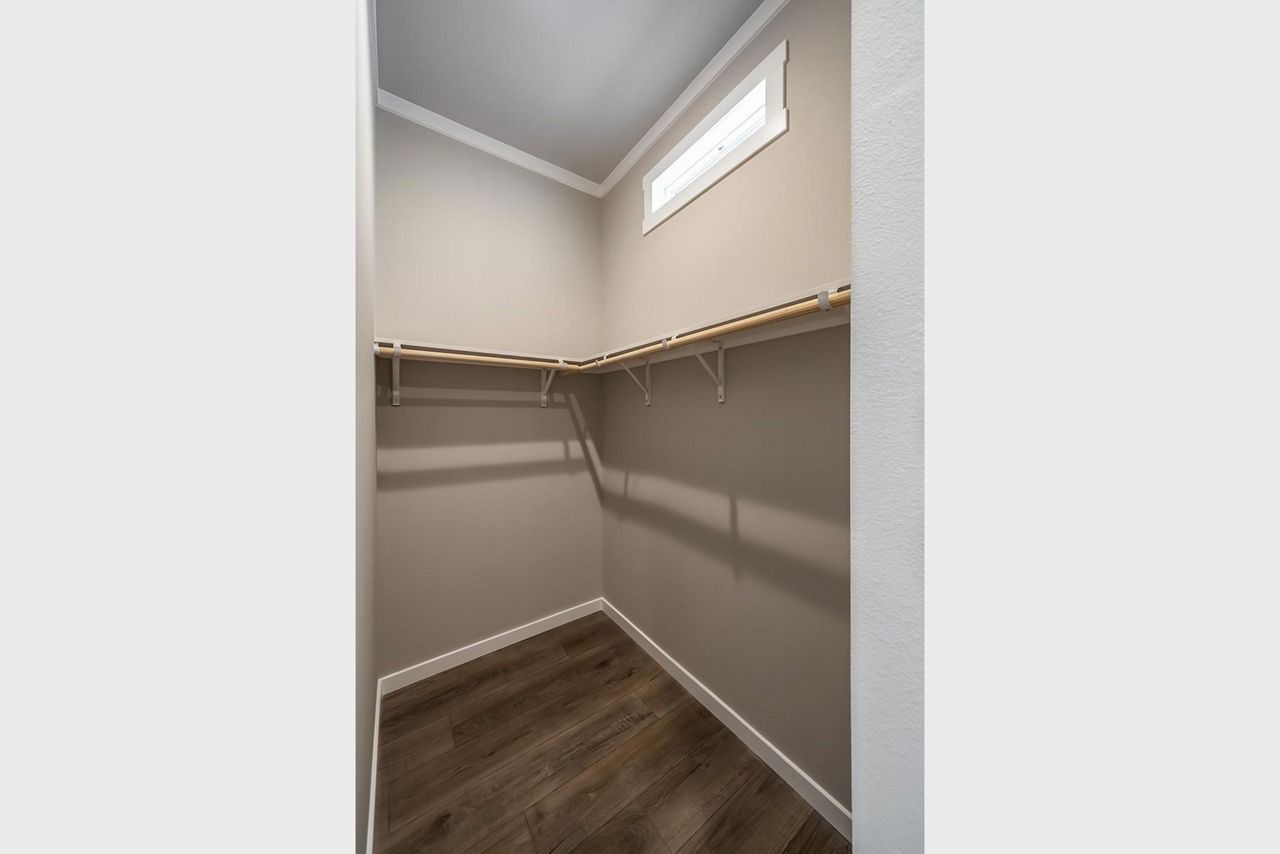 Empty walk-in closet with beige walls, white shelves, and dark wood flooring