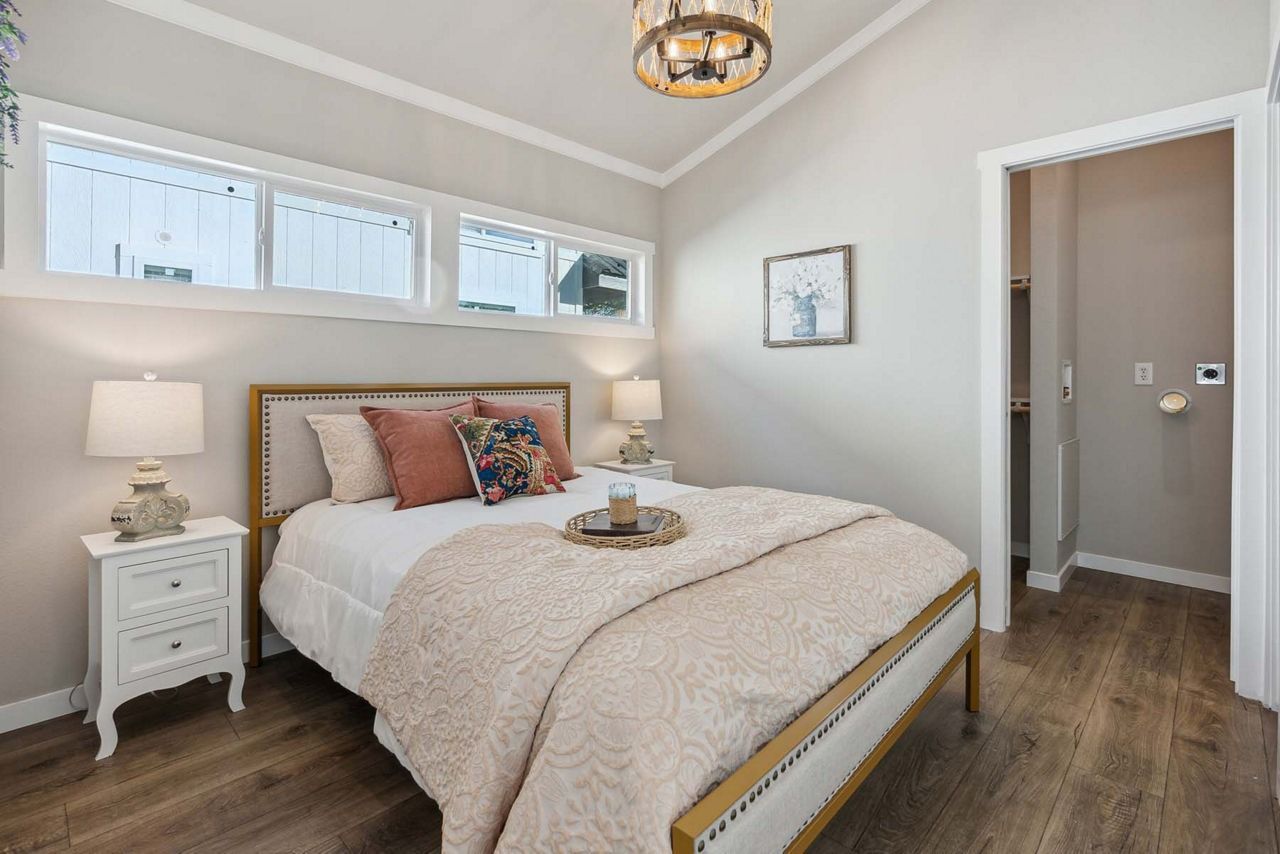 Bright bedroom with white walls, wooden bed, bedside lamp, and hardwood floors.