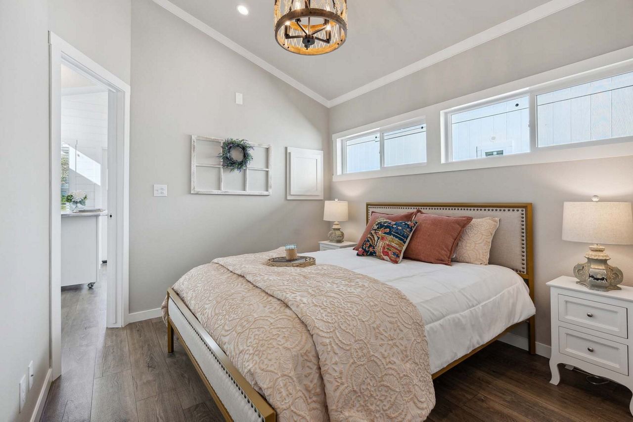 Bright bedroom with a bed, nightstands, and three windows on light gray walls