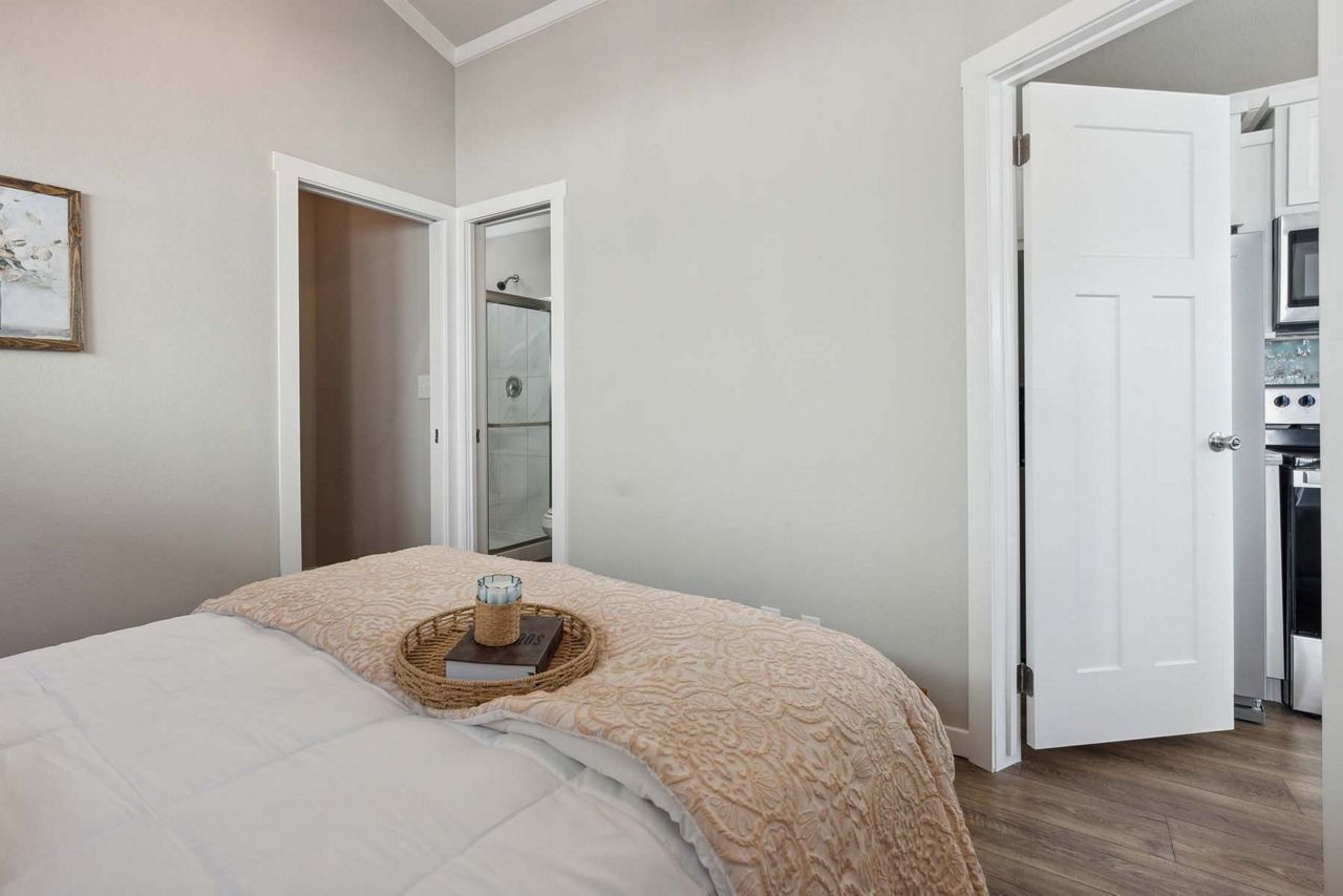 Neat bedroom with a made bed, light walls, and an open doorway to a bathroom and closet.