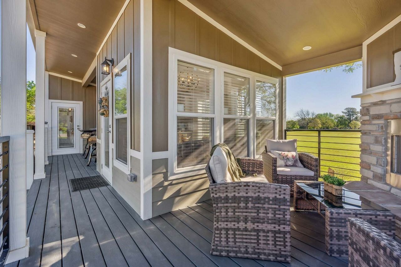 Covered porch with wicker seating, gray deck boards, and a view of green fields