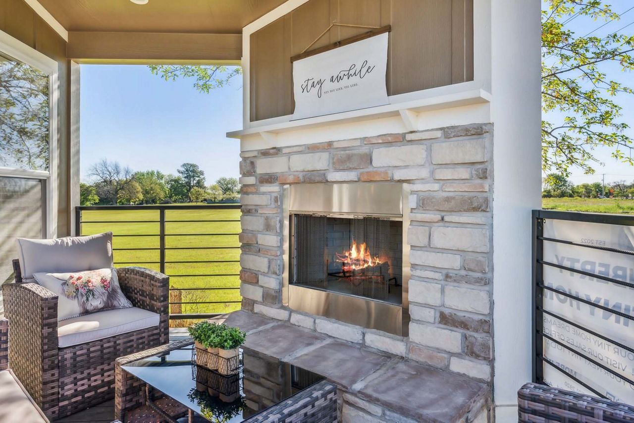 Covered patio with stone fireplace, wicker chairs, and a view of green lawn and trees