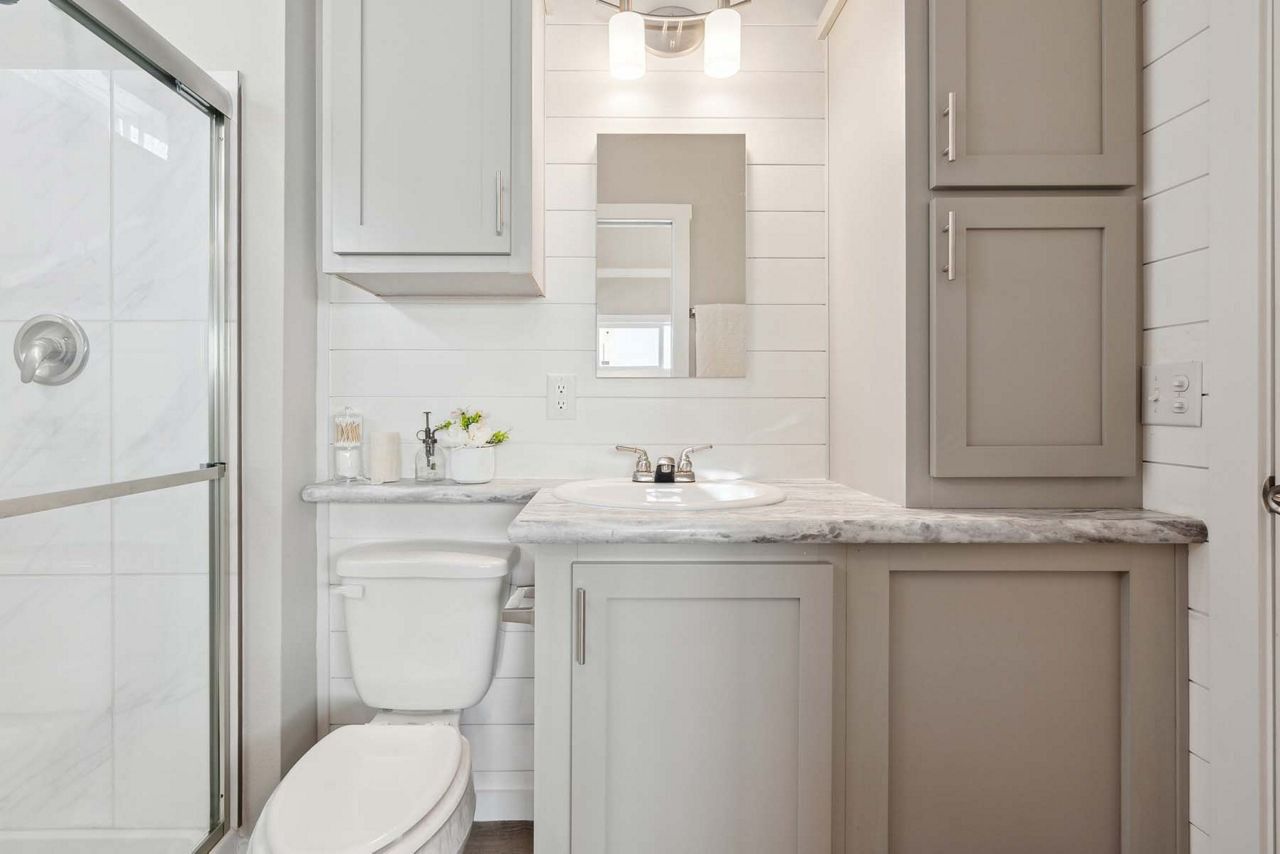 Small white bathroom with vanity, toilet, and mirror beside a shower stall.