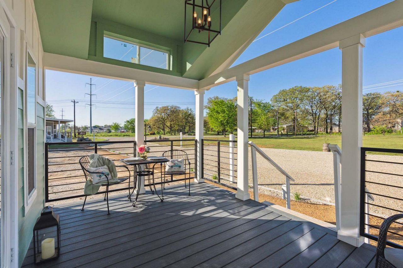 Covered porch with wicker chairs and a table overlooking a grassy yard and trees