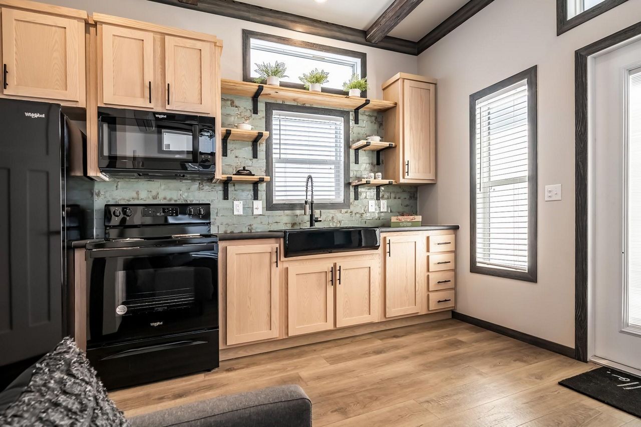 Modern kitchen with black appliances, light wood cabinets, and a window over the sink