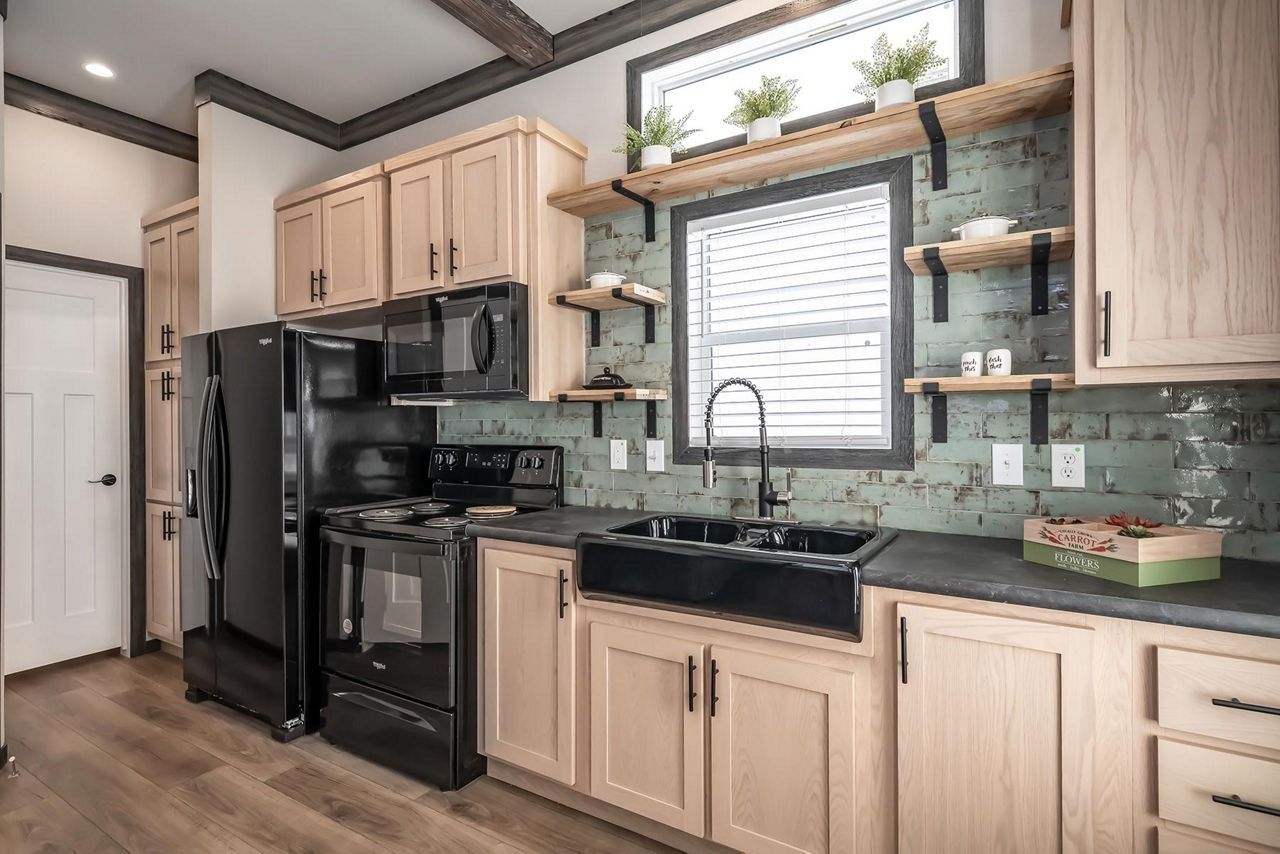 Modern kitchen with black appliances, light wood cabinets, and a window above the sink