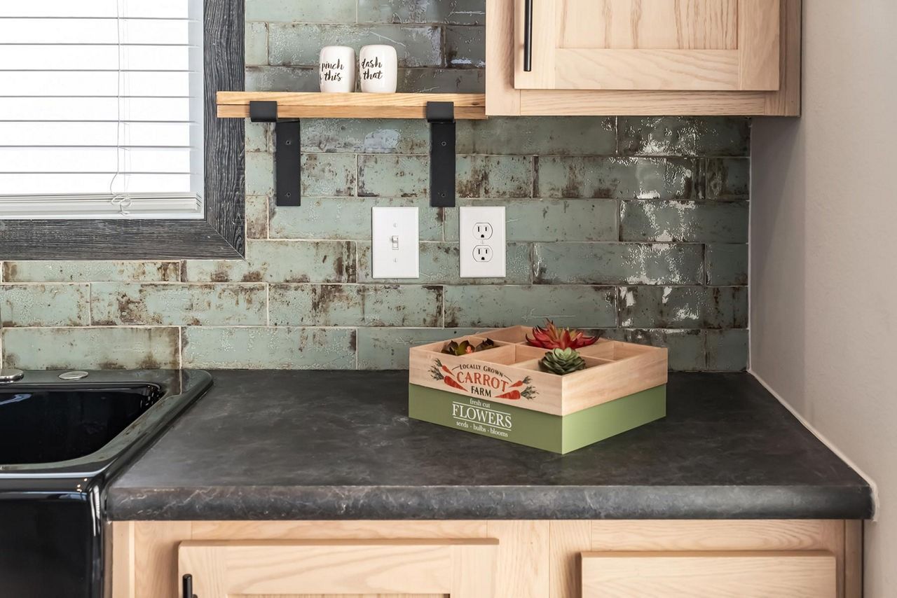 Kitchen counter with black countertop, tiled backsplash, outlet, and a small box of strawberries.