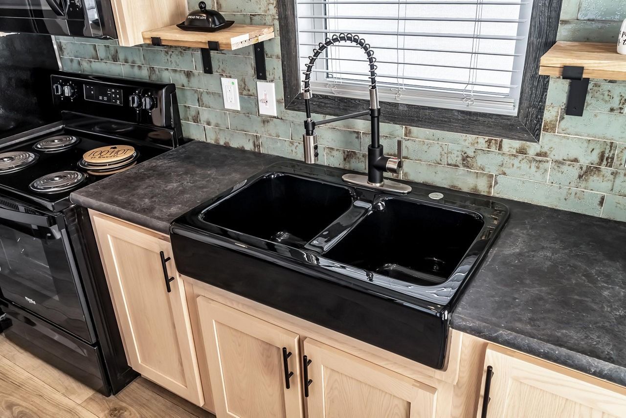Kitchen sink and black countertop beside a stove, with a window above the faucet.