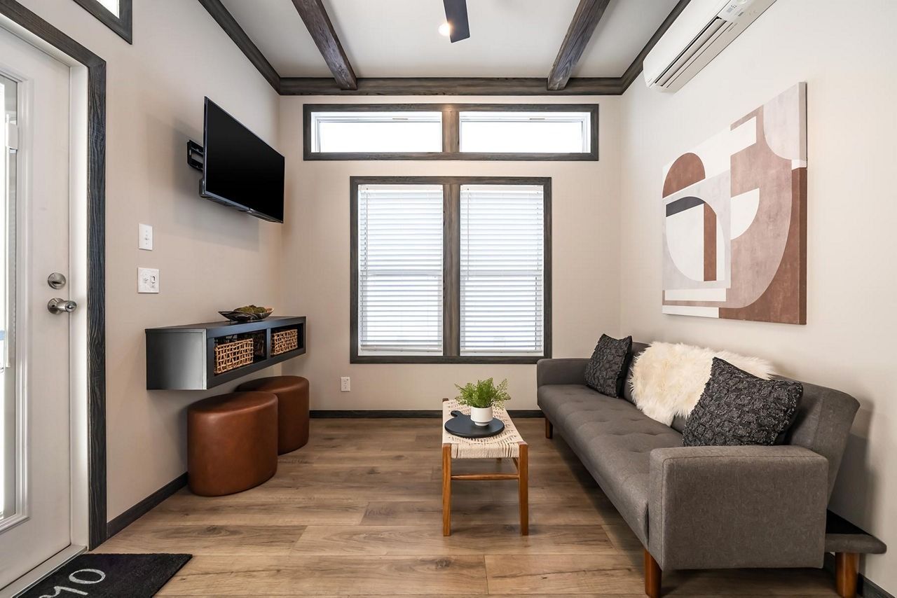 Modern living room with gray sofa, wall TV, window blinds, and small coffee table under abstract art.