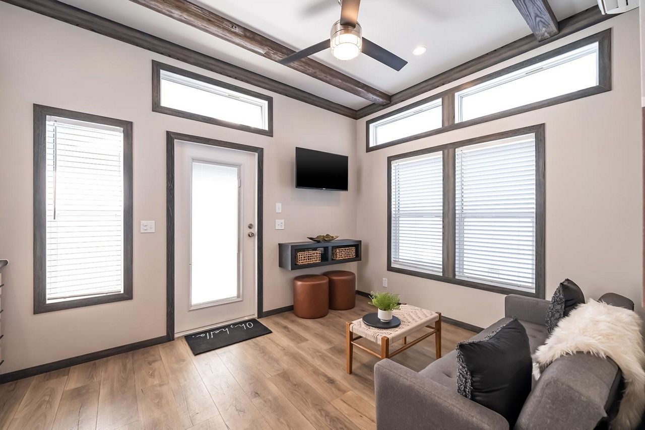 Bright living room with high windows, TV, ceiling fan, sofa, and wood floors