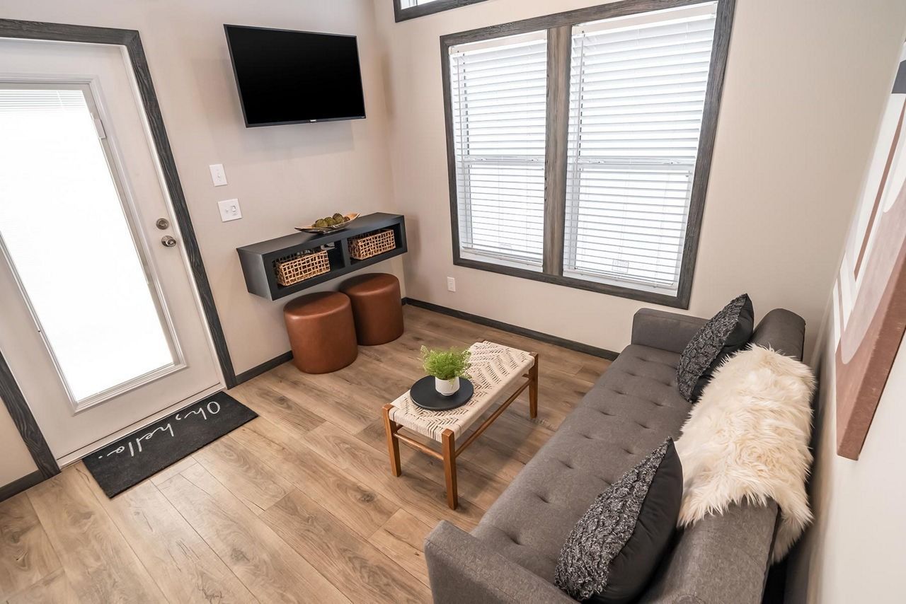 Small living room with gray sofa, coffee table, wall-mounted TV, window, and front door.