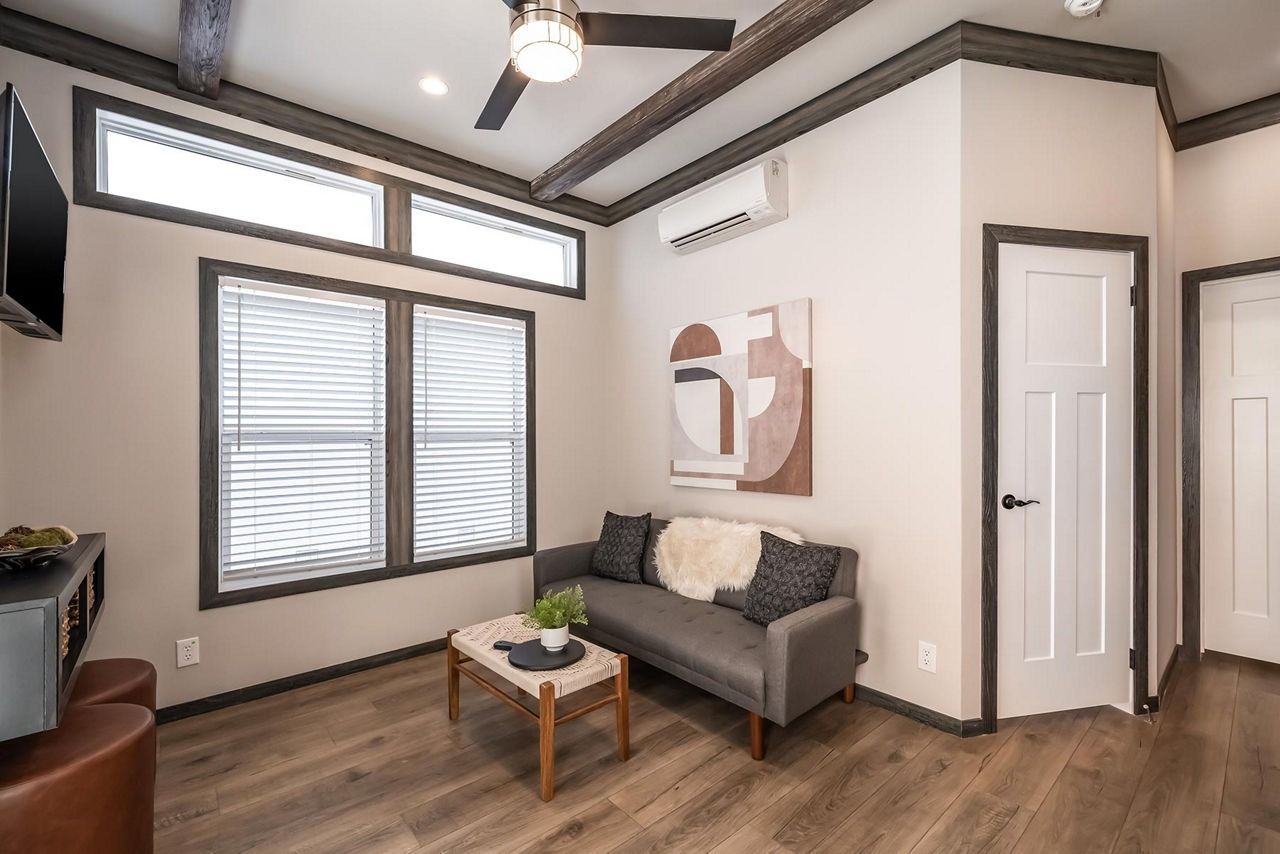 Bright modern living room with gray sofa, wood floors, large windows, and white walls with dark trim