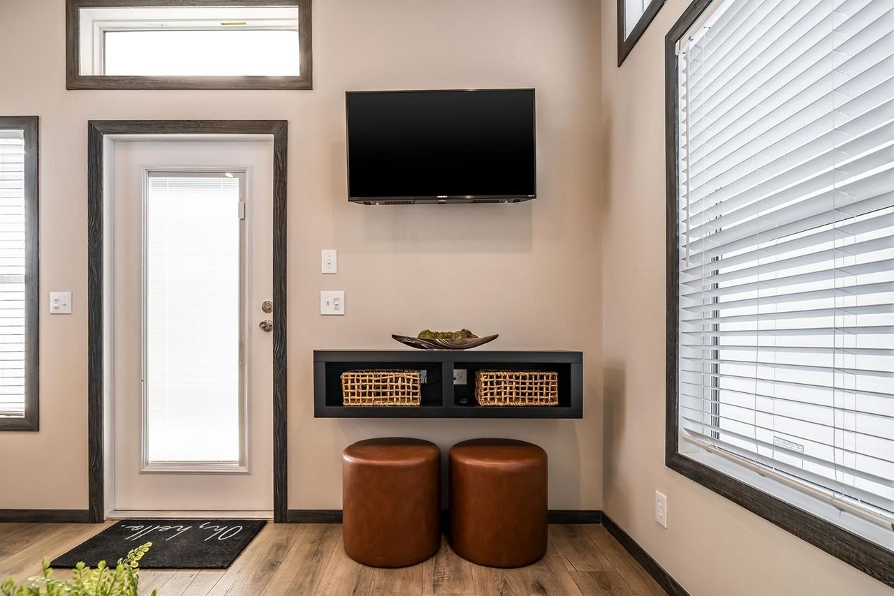 Small entryway with a wall-mounted TV, narrow console, two brown stools, and a glass front door.