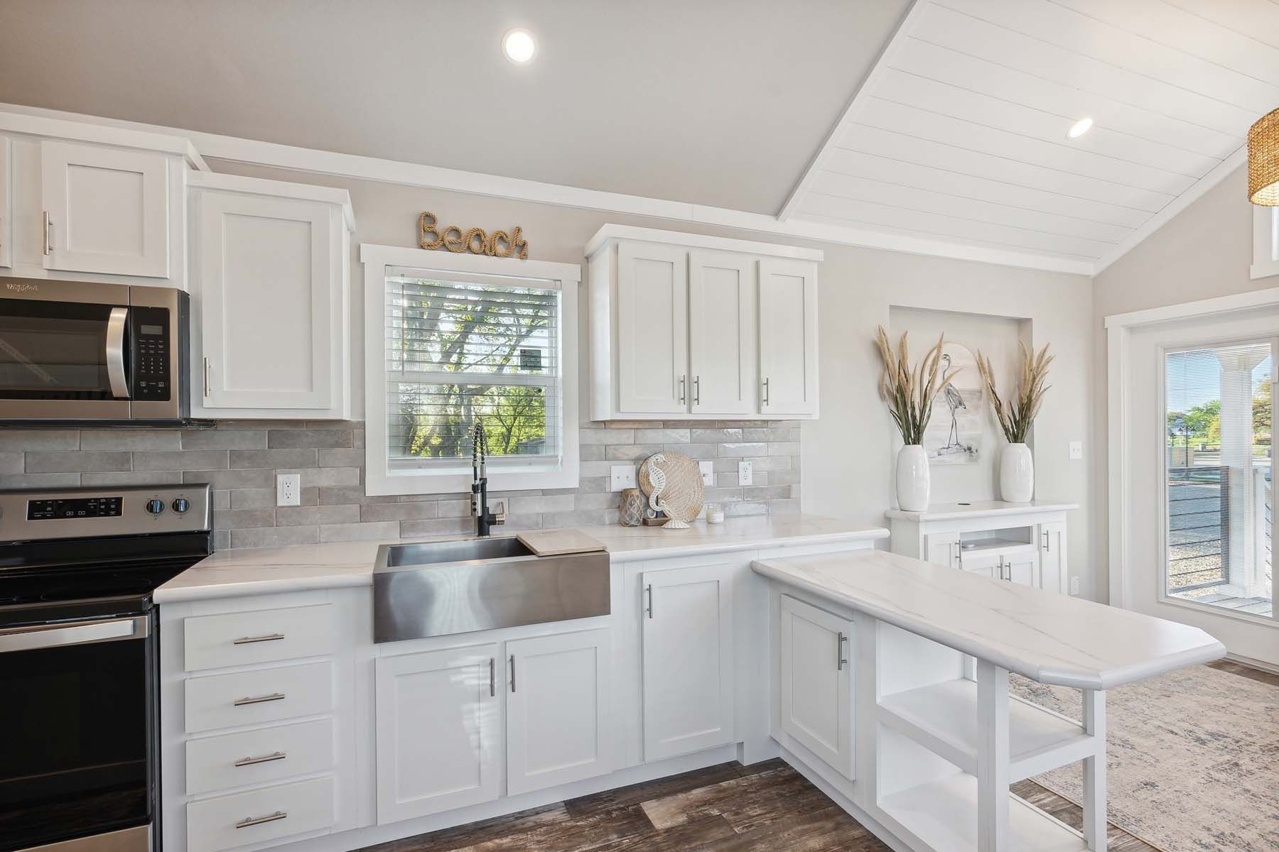 Bright white kitchen with farmhouse sink, island, stainless appliances, and sliding glass door