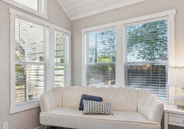 Bright sunroom with beige sectional sofa, large windows, tile floor, and brick accents overlooking trees