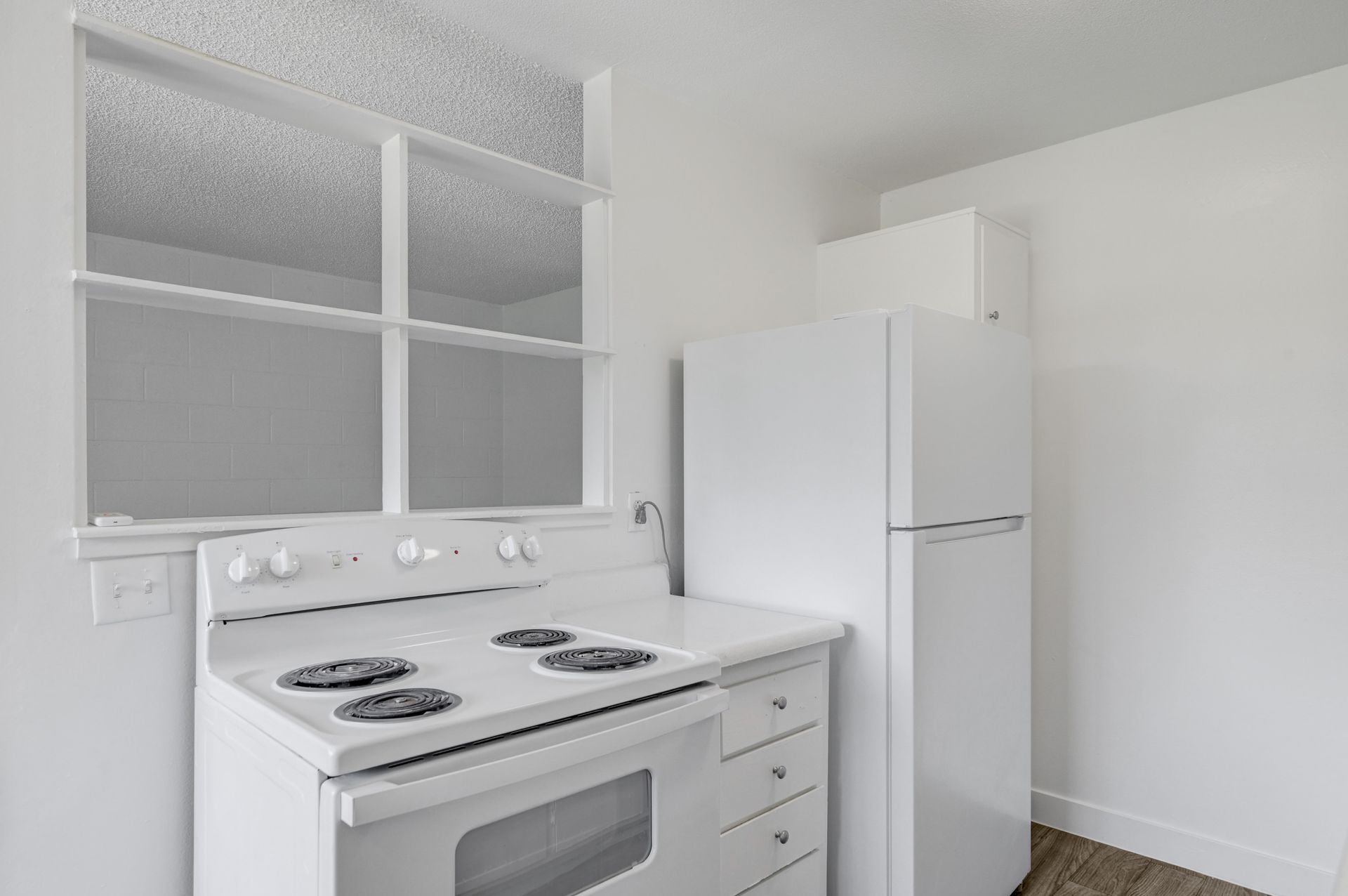 Bright white kitchen with a stove, refrigerator, and window above the counter.