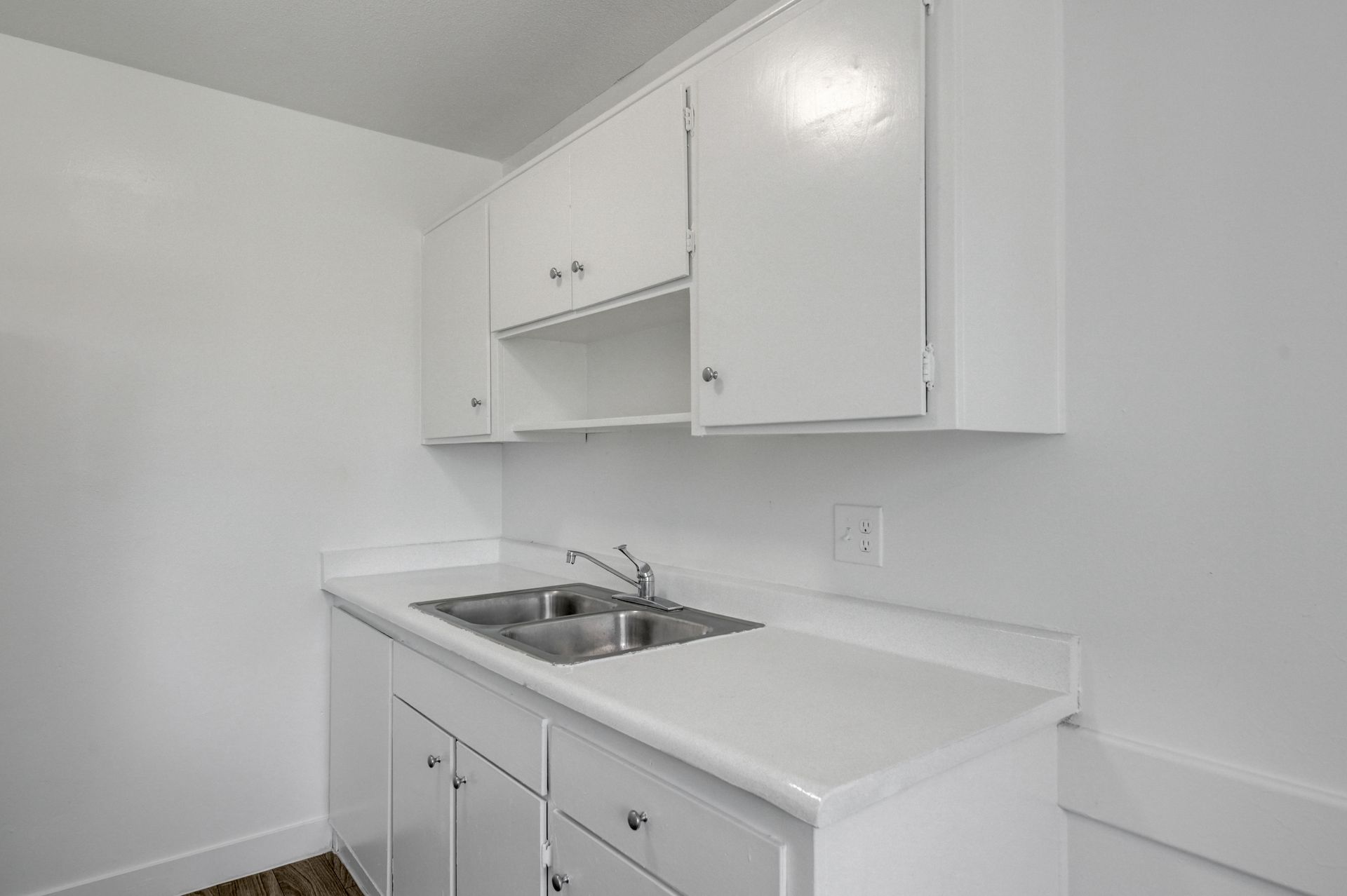 Small white kitchen with sink, cabinets, and countertop against a plain wall