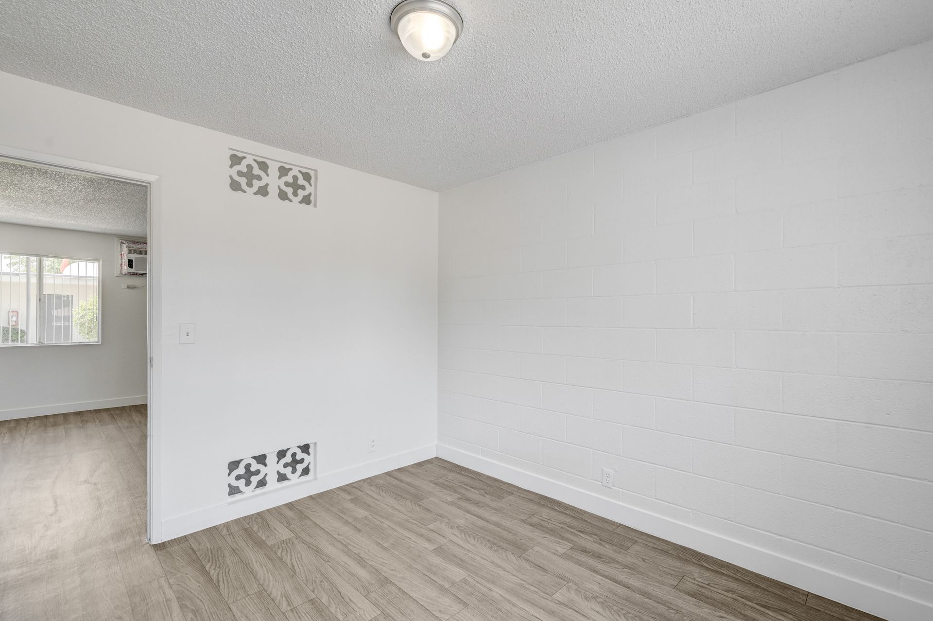 Empty white room with wood-look flooring, a ceiling light, and decorative wall vents