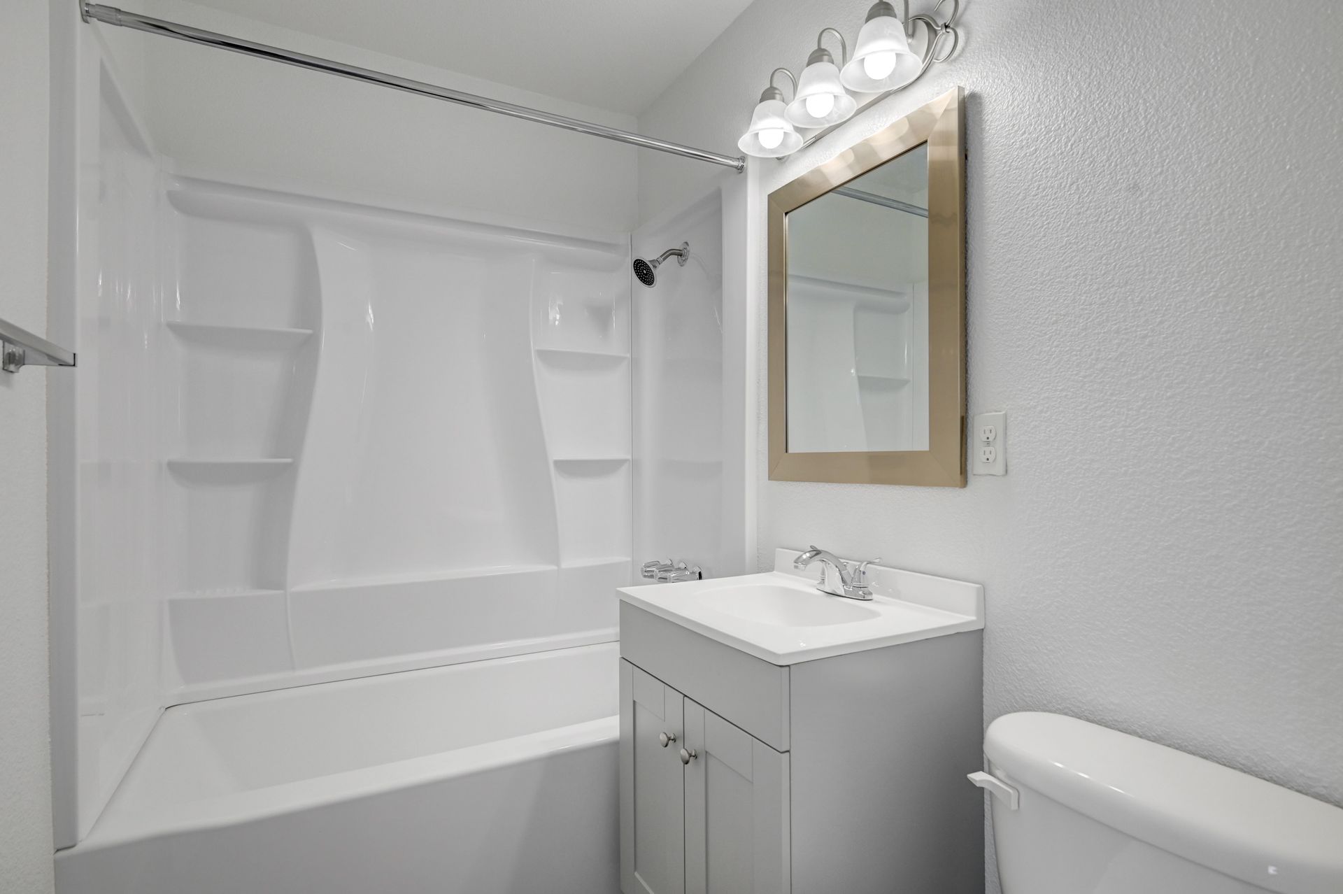 Small white bathroom with a tub-shower, sink vanity, mirror, and toilet