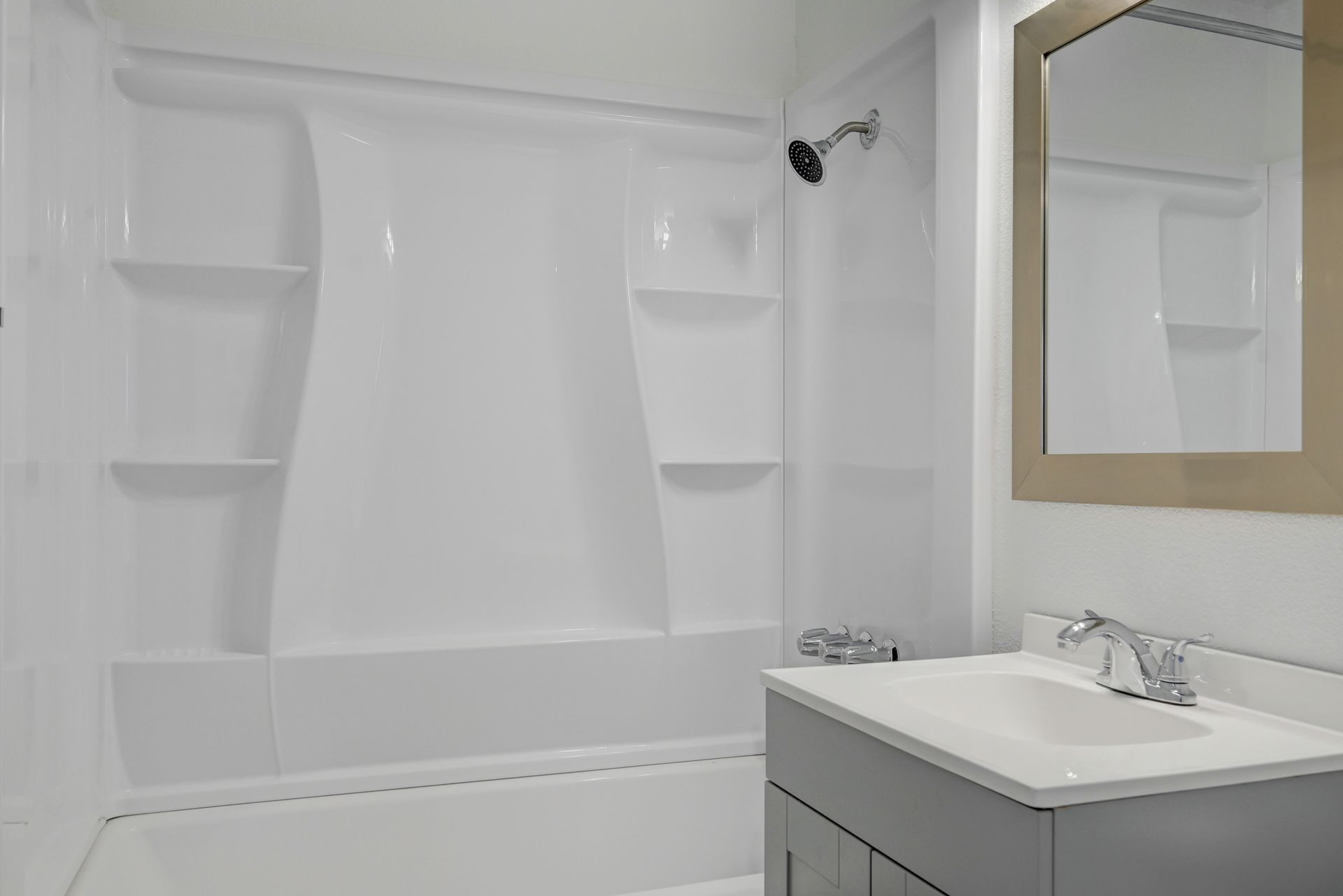 White bathroom with a tub-shower, built-in corner shelves, and a vanity sink mirror