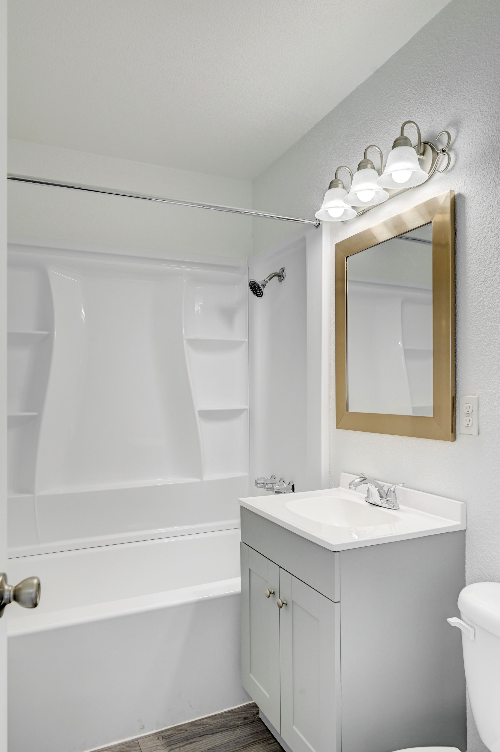 Small white bathroom with tub-shower combo, vanity sink, mirror, and overhead lights.