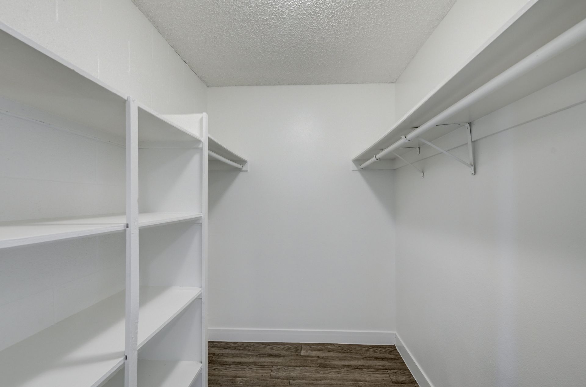 Empty white walk-in closet with shelves and hanging rods, wood floor, and a slanted ceiling