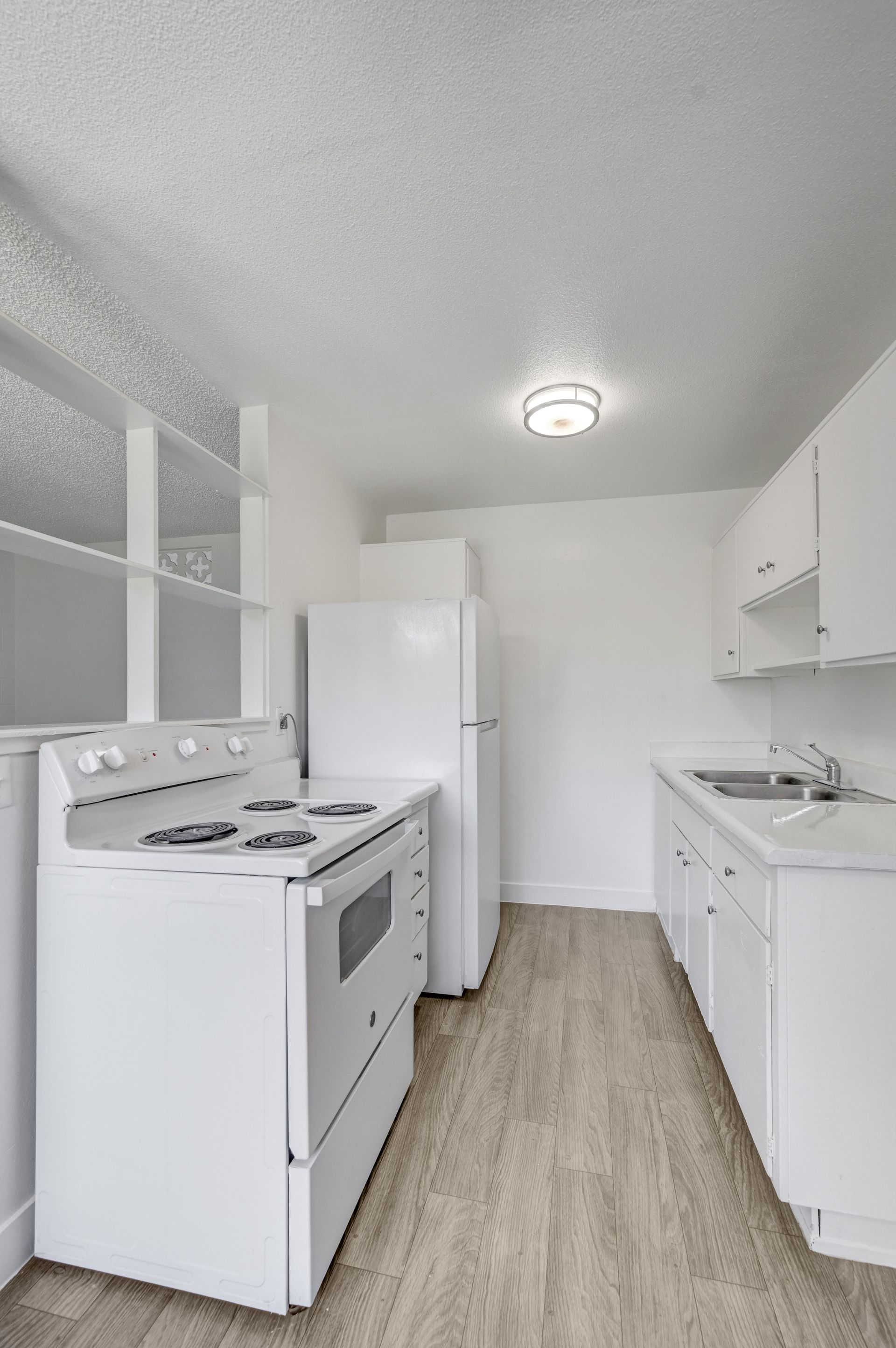 Small white kitchen with stove, refrigerator, cabinets, and light wood floor