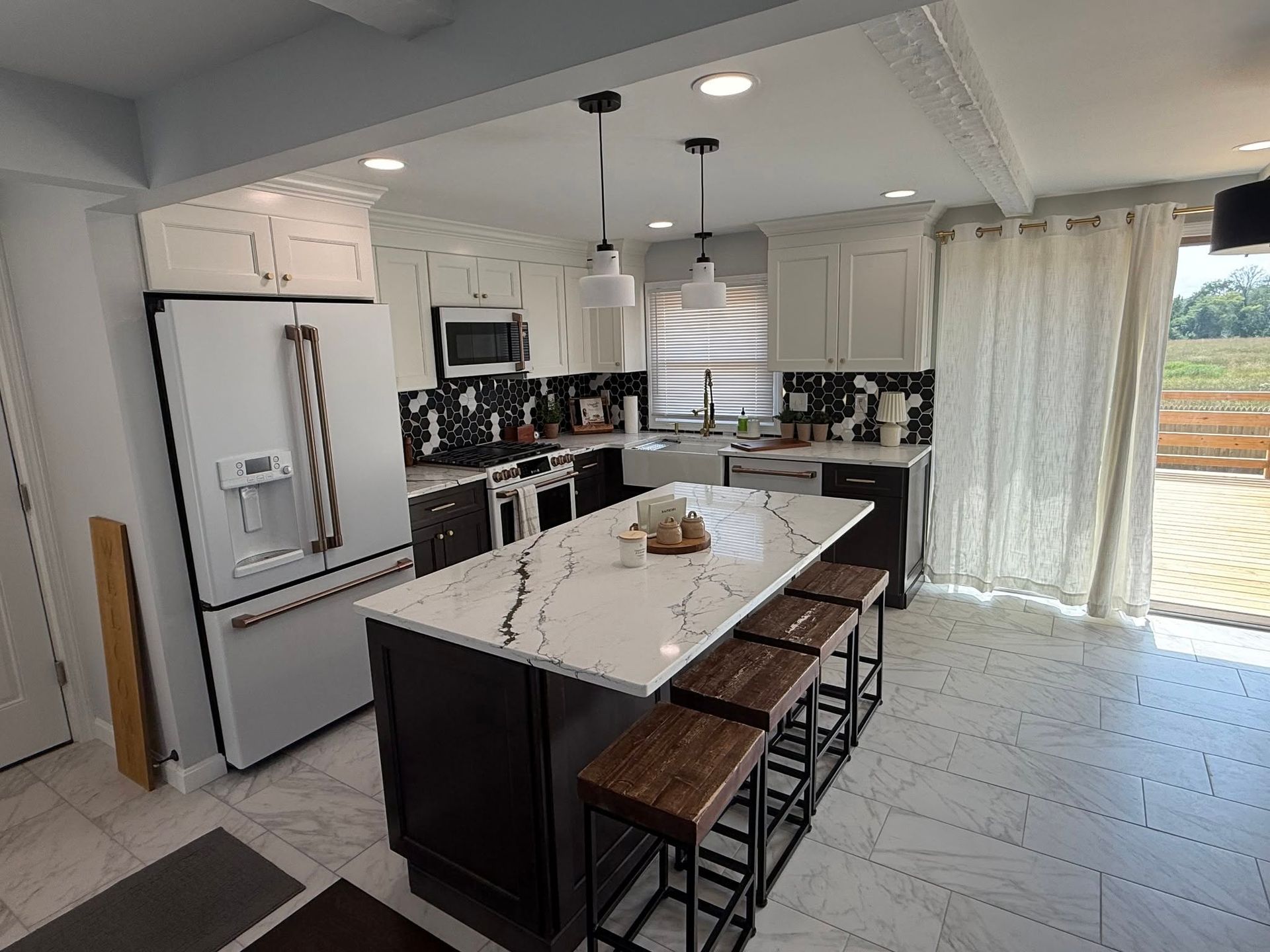 Client kitchen with a white veined countertop island, dark base cabinets and stool seating