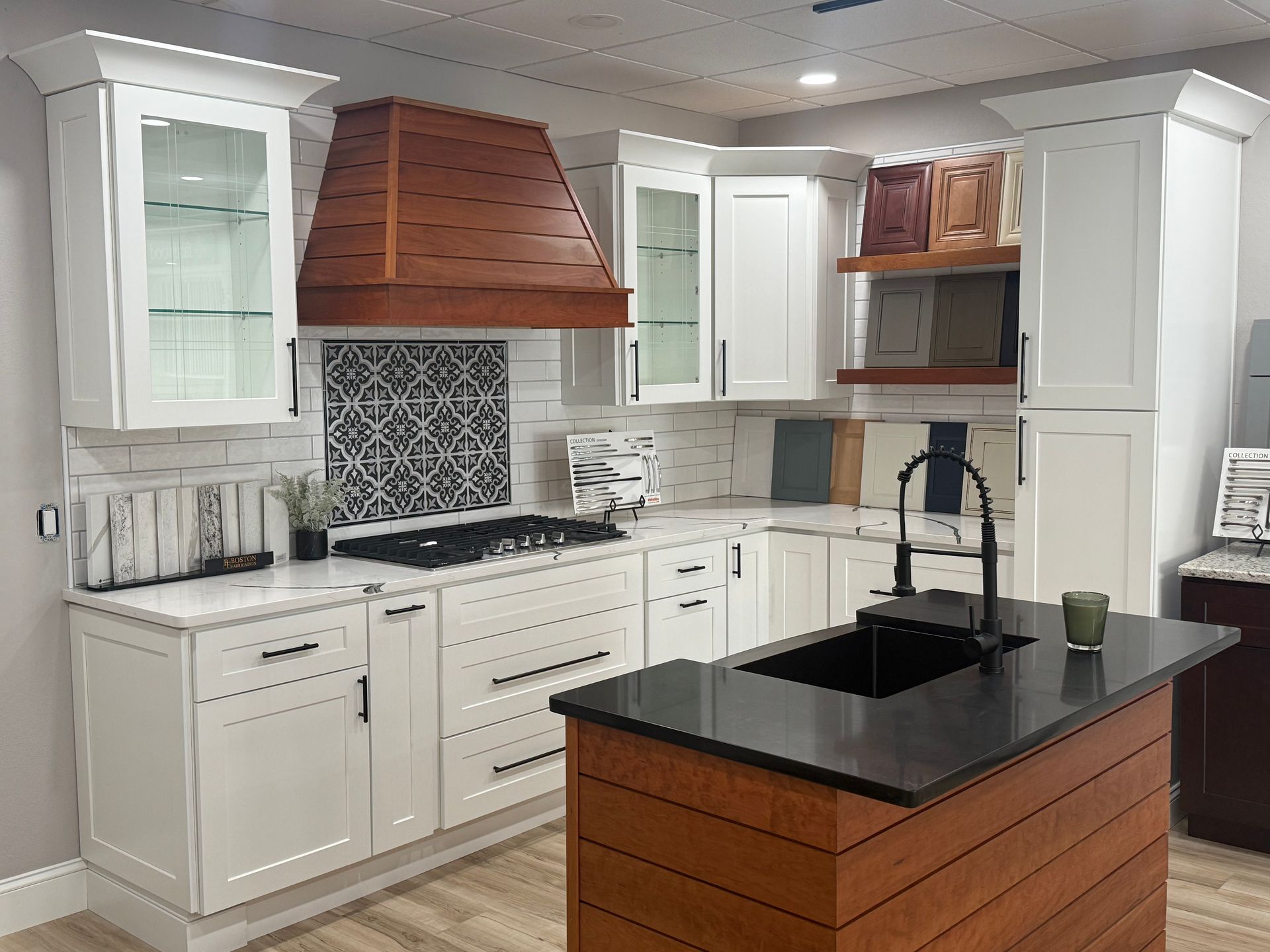 Kitchen display at Darlington Kitchen & Bath’s Pawtucket showroom, with white cabinetry, a wood hood and a dark countertop island