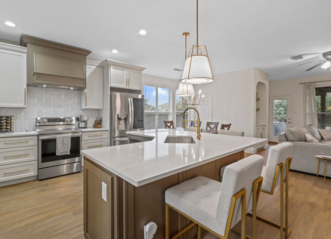 A modern kitchen featuring white cabinets, stainless steel appliances, a marble-topped island, and two grey bar stools.