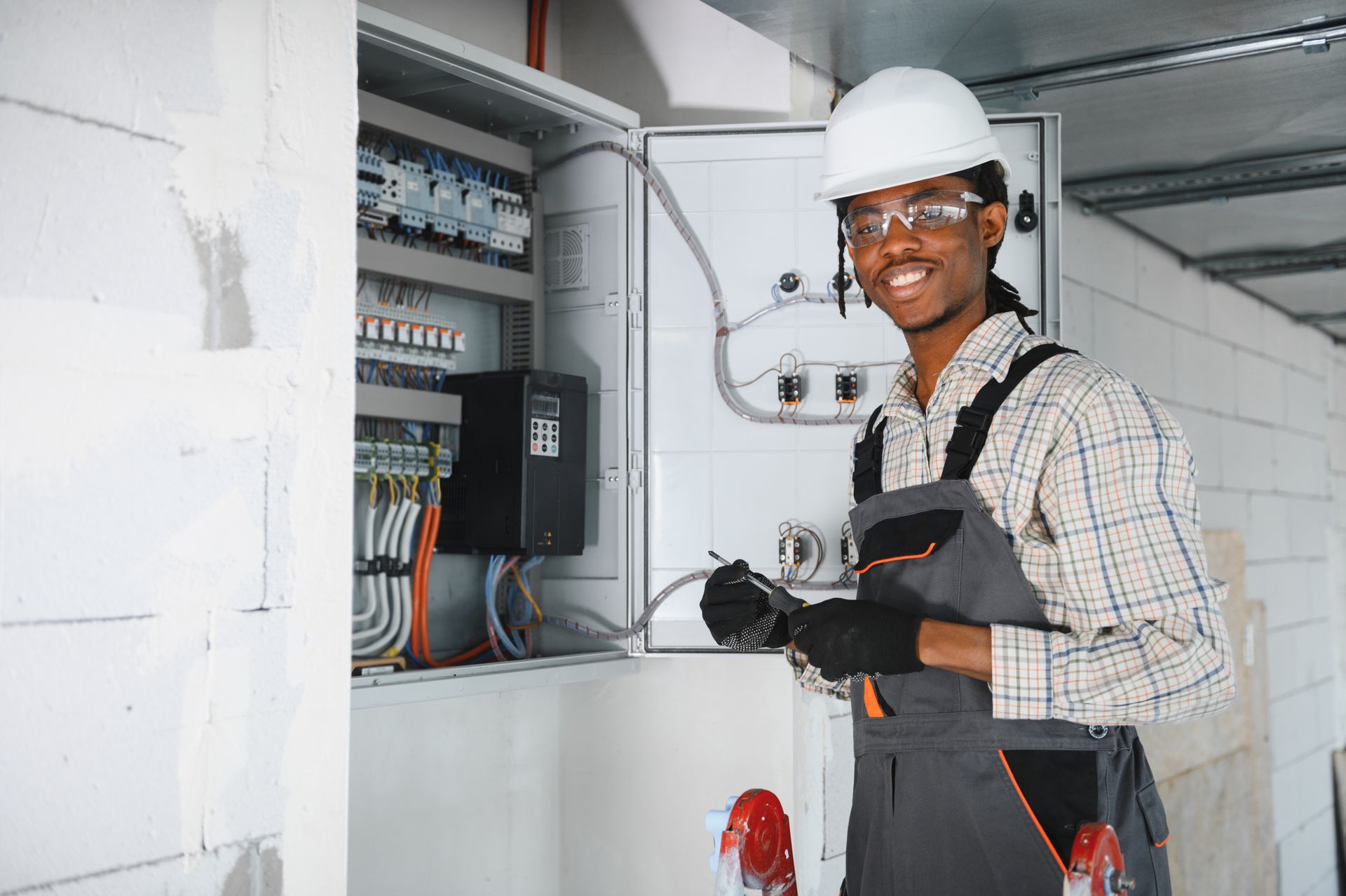 Commercial electrician working on control panel in building under construction. Electrician in hard hat inspecting an open electrical panel with tools in hand