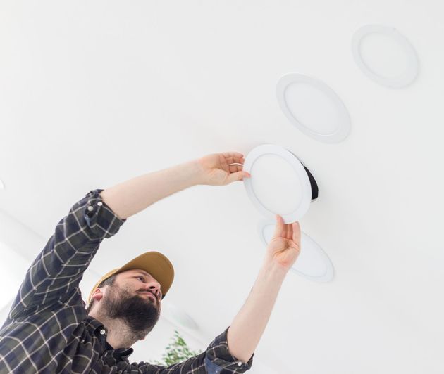 Man installing a round ceiling light fixture against a white ceiling