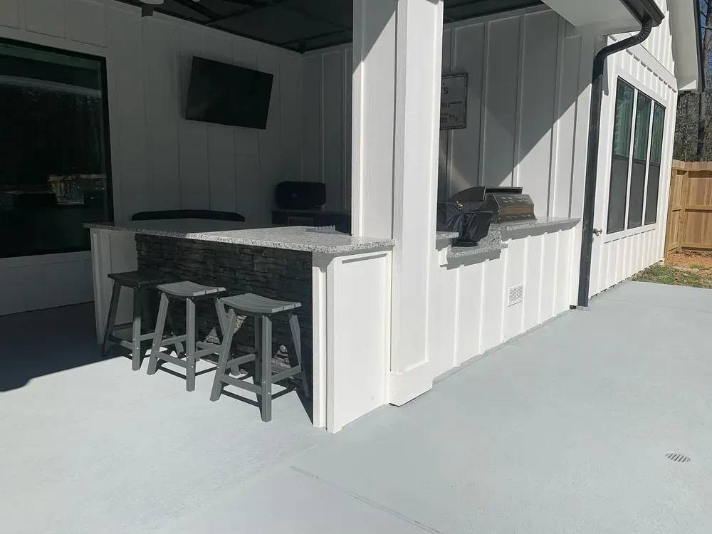 A white house with a covered patio with a bar and stools.