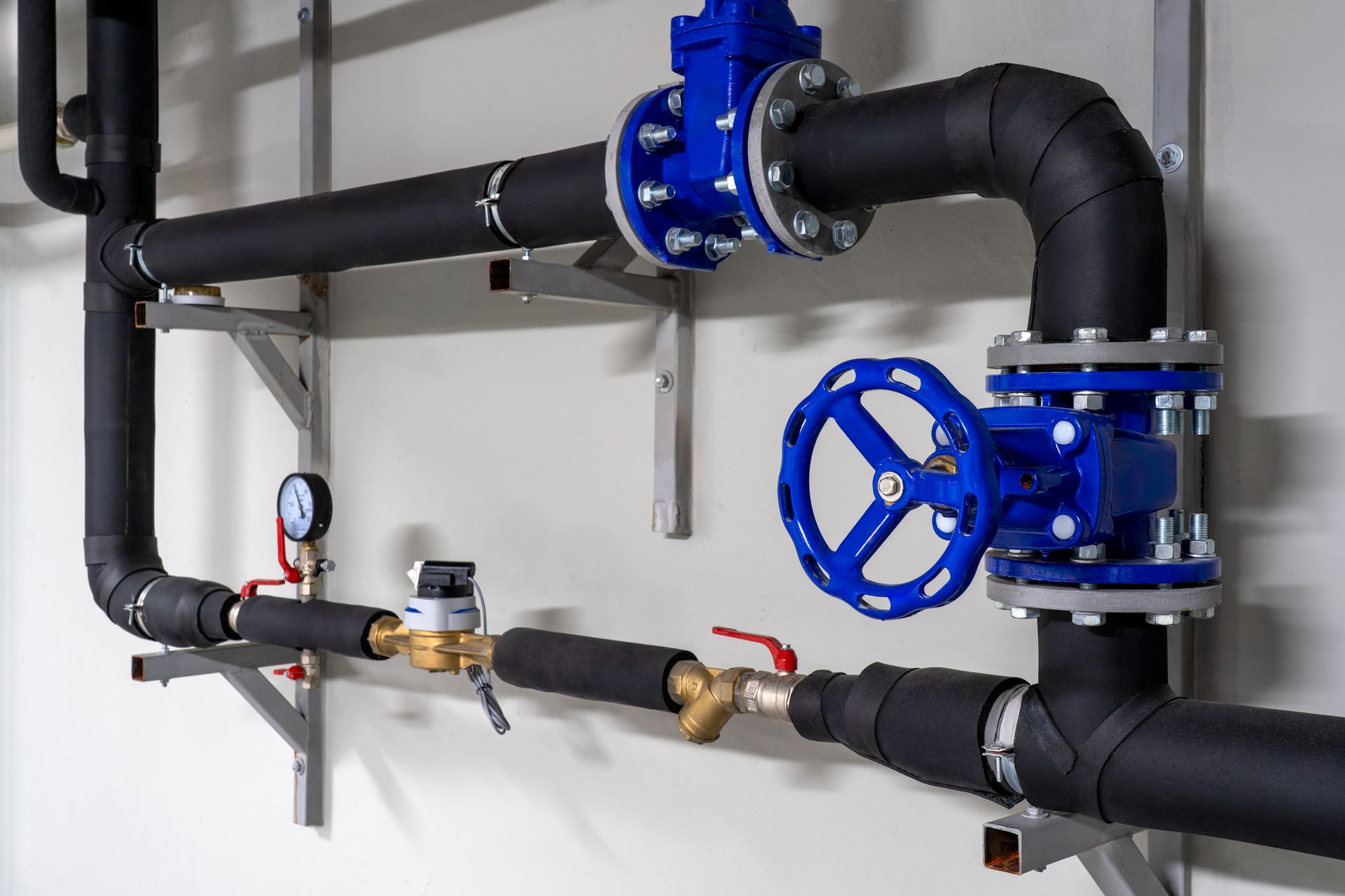 Insulated commercial plumbing pipes with blue gate valves, gauge and water meter.