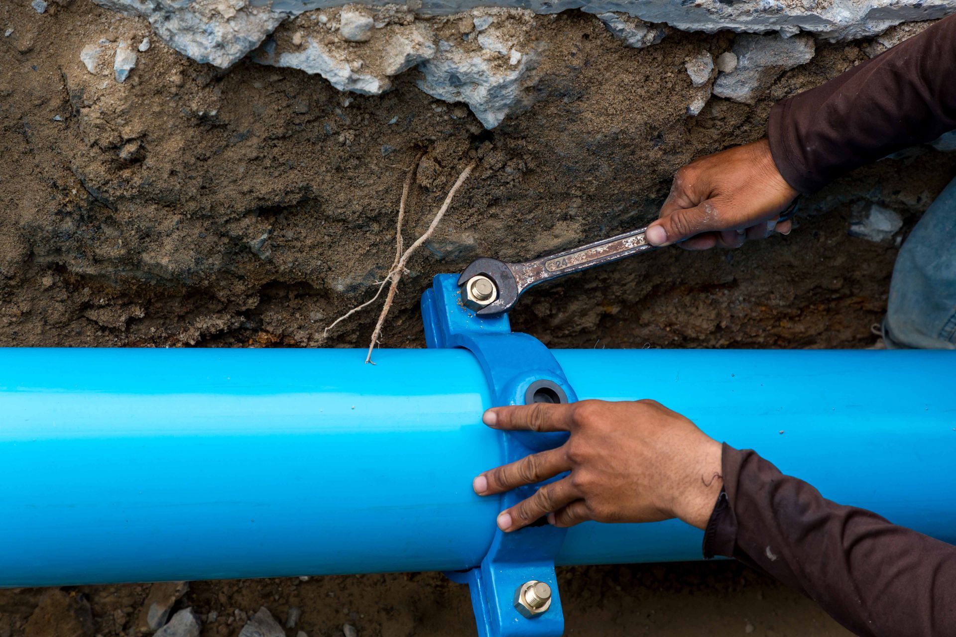 Technician repairing underground pipe with wrench during water line services installation work. Technician repairing underground pipe with wrench during water line services installation work.