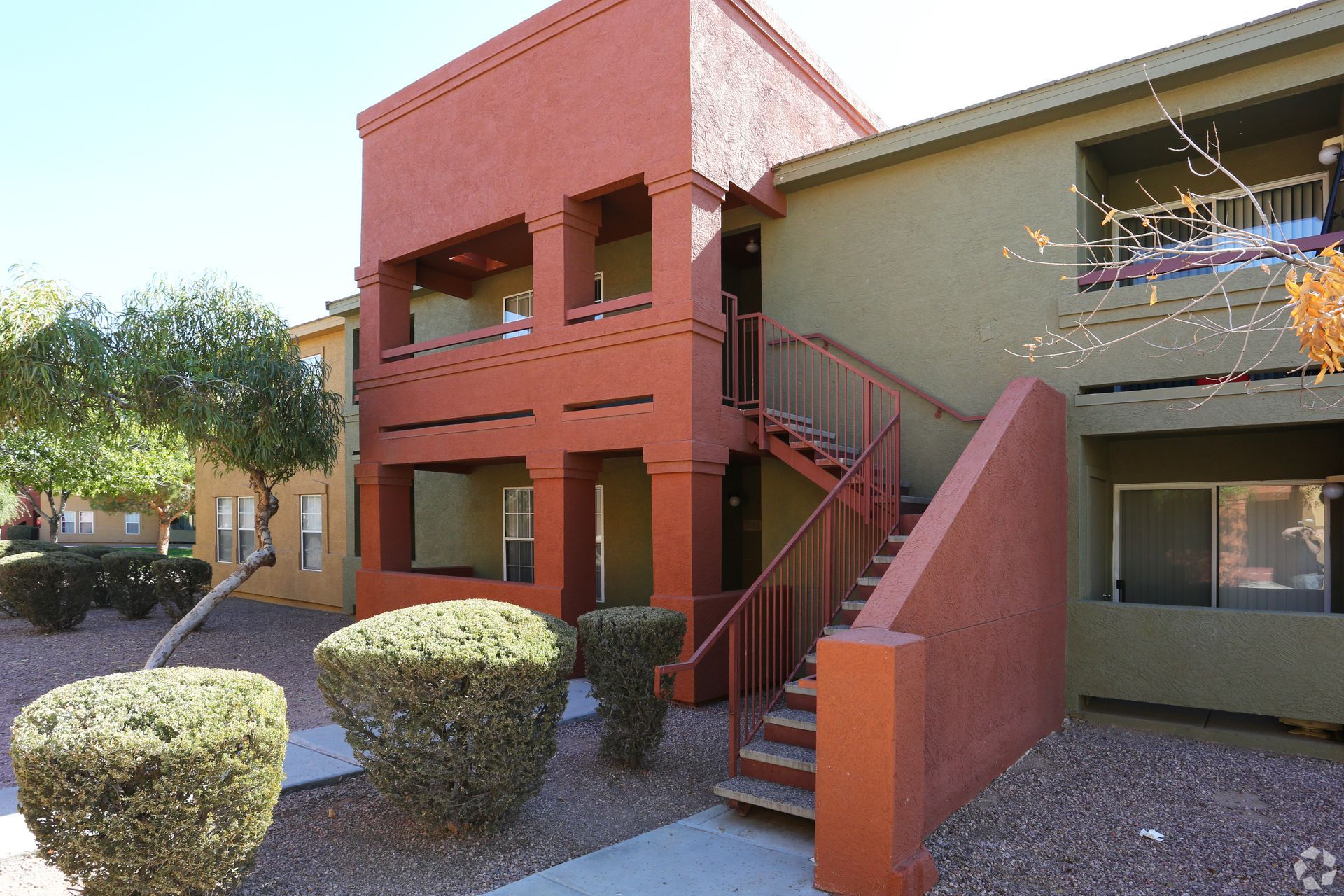 A two-story apartment building with a terracotta-colored entrance, olive green siding, and an outdoor staircase.