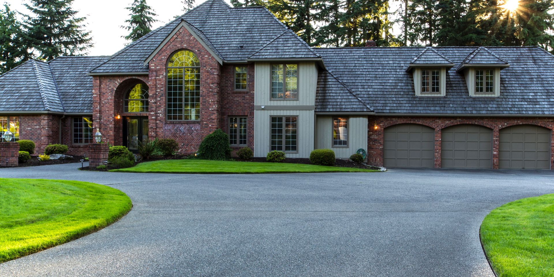Large modern brick house with gray roof, three-car garage, and a curved driveway at dusk
