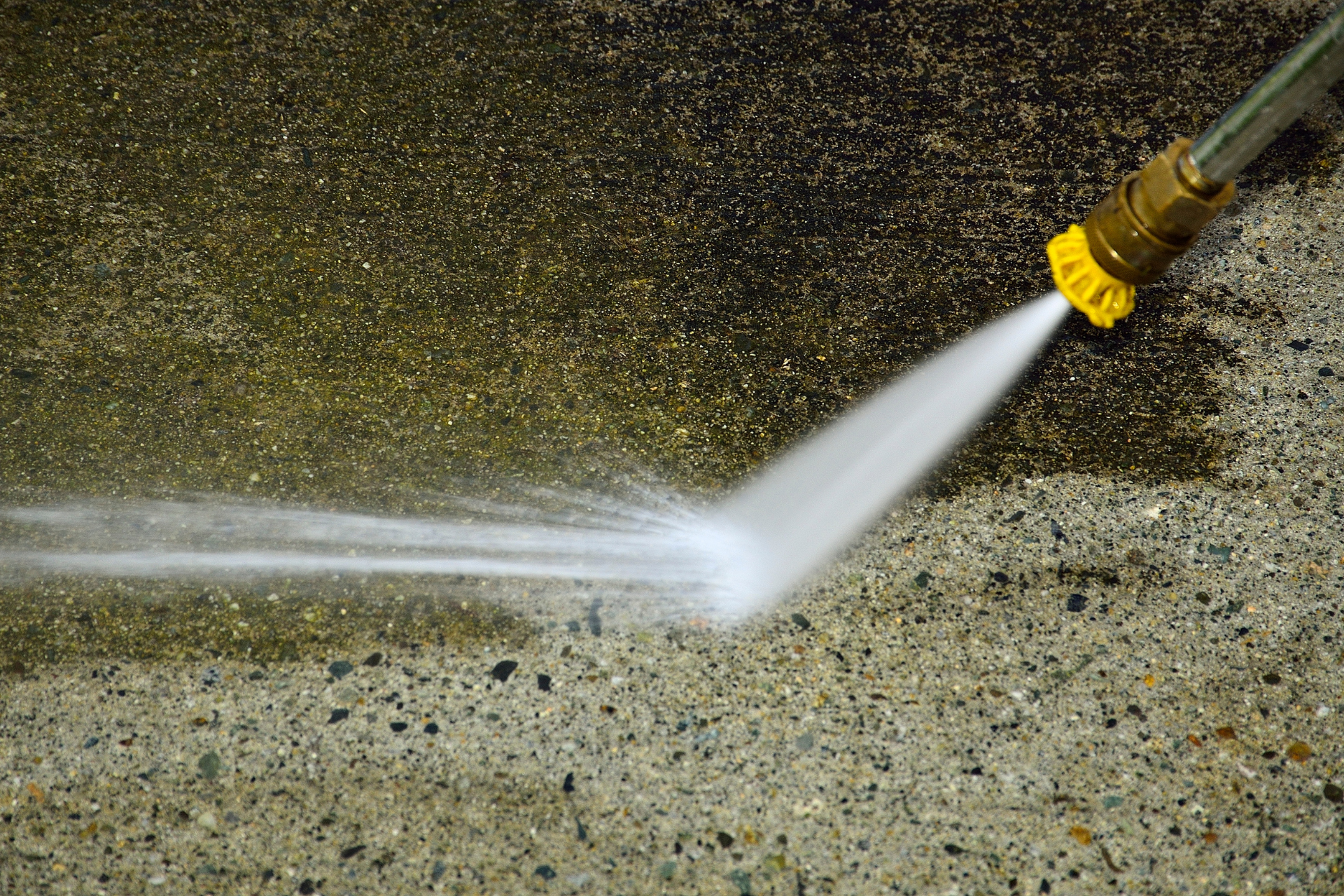 Pressure washer spraying a concrete wall, blasting dirt off the surface