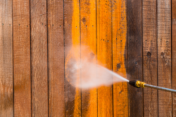 Pressure washer spraying a wooden fence, cleaning a section of orange-stained boards