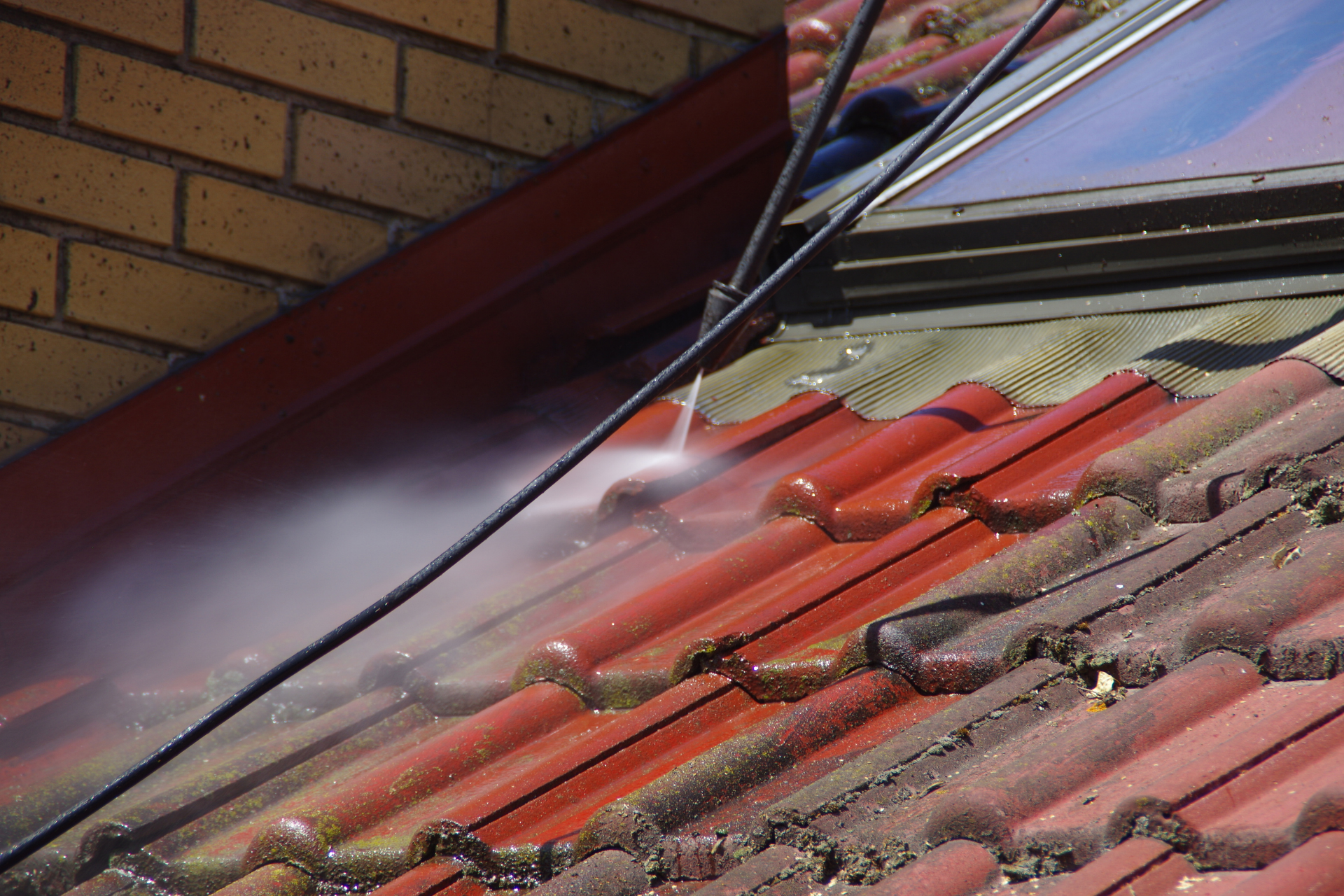 Water spraying onto red roof tiles beside a brick wall, likely cleaning or repairing a roof