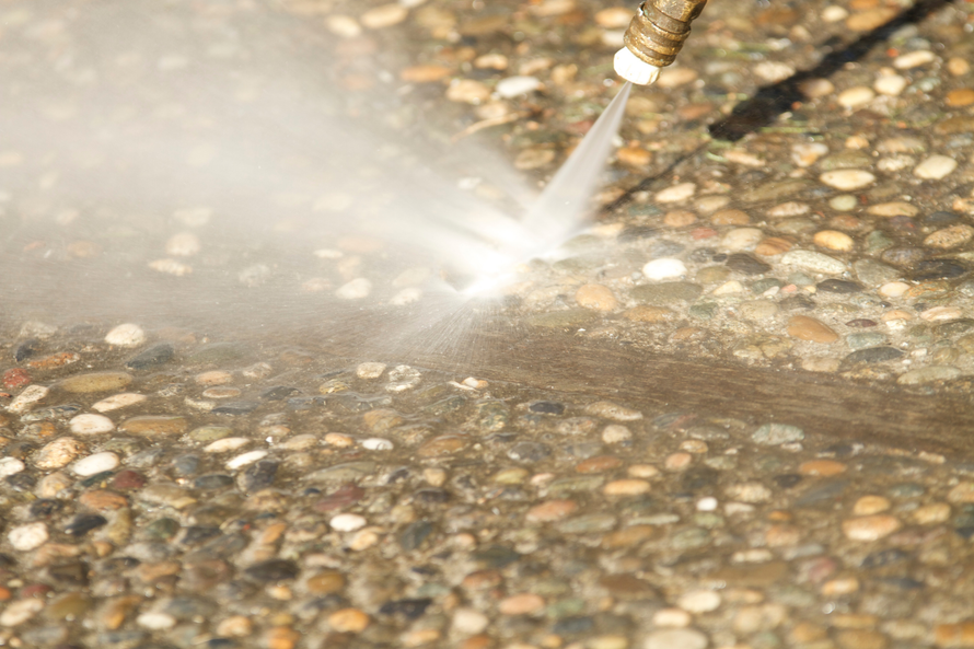 Pressure washer cleaning a pebble-textured surface with a strong water spray